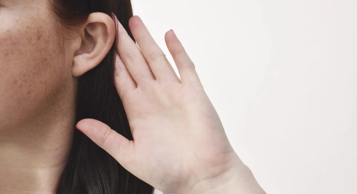 A person holding their hand up to their ear, appearing to listen carefully.
