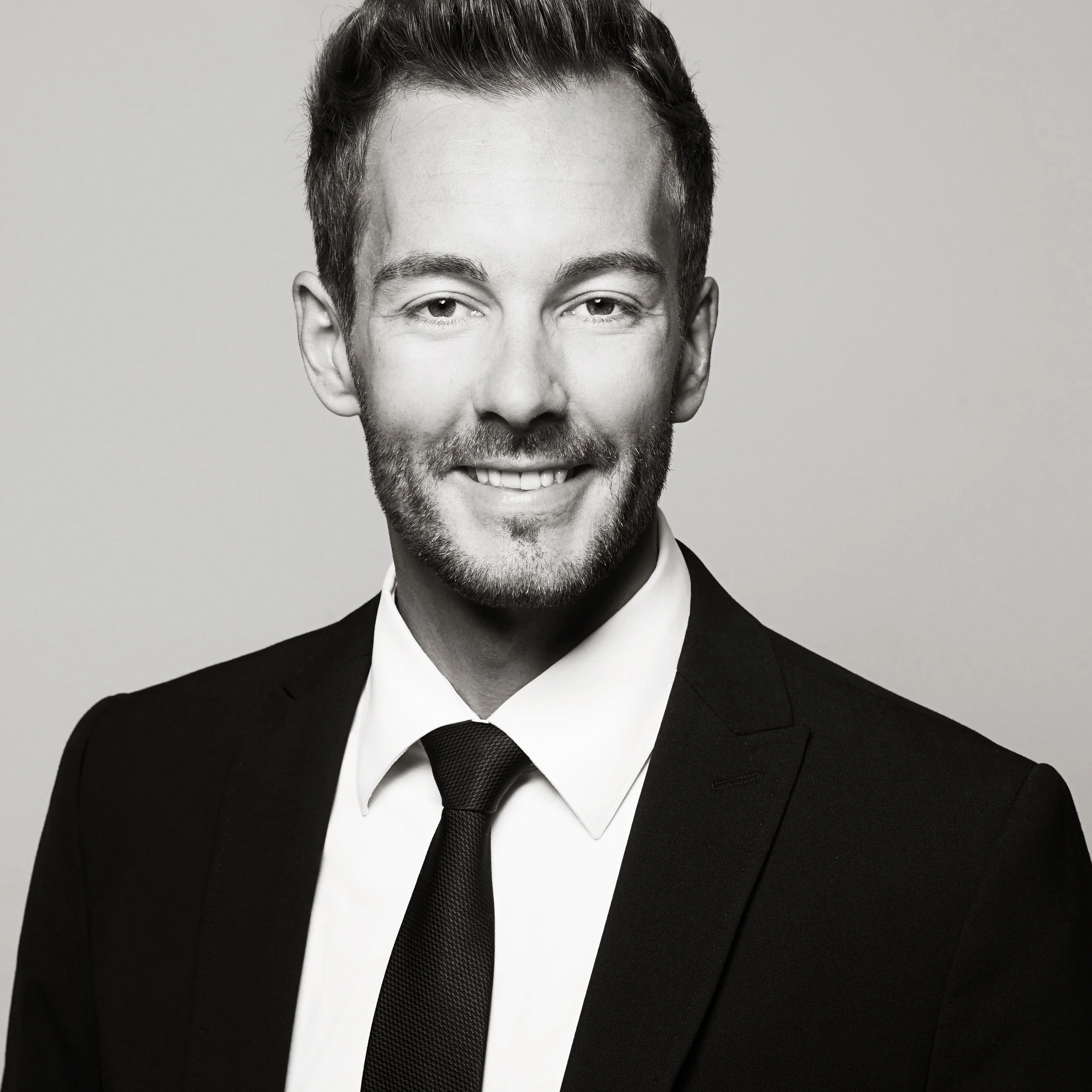 A black and white portrait of a smiling man in a suit and tie.