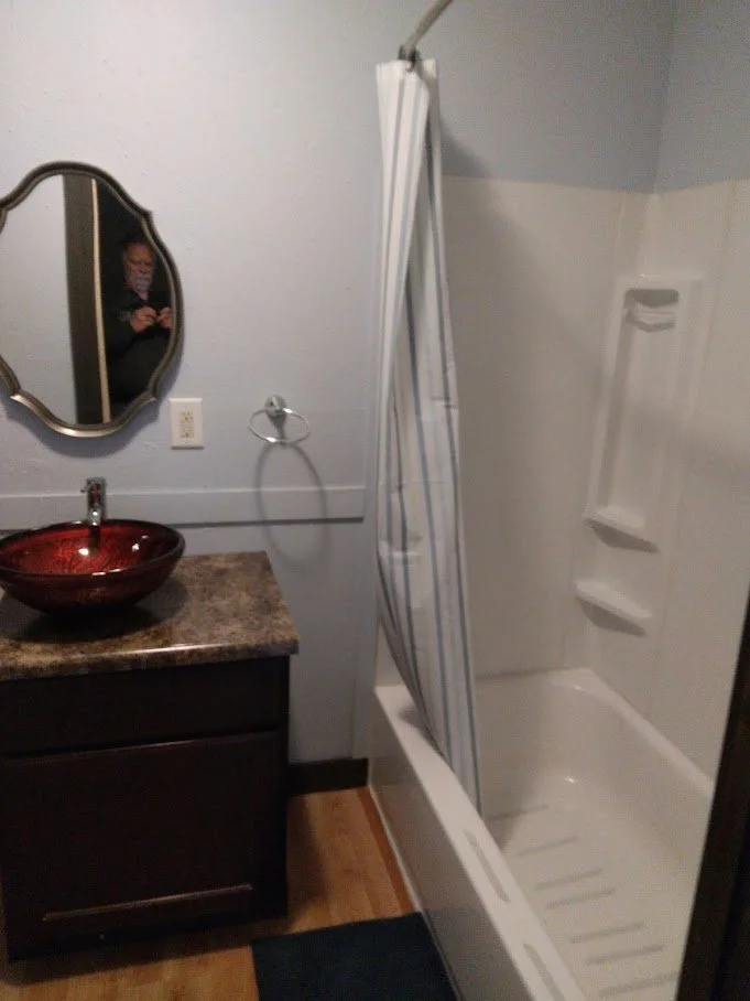 Bathroom with a vanity, a red vessel sink, a mirror, a shower with a striped curtain, and a handrail.