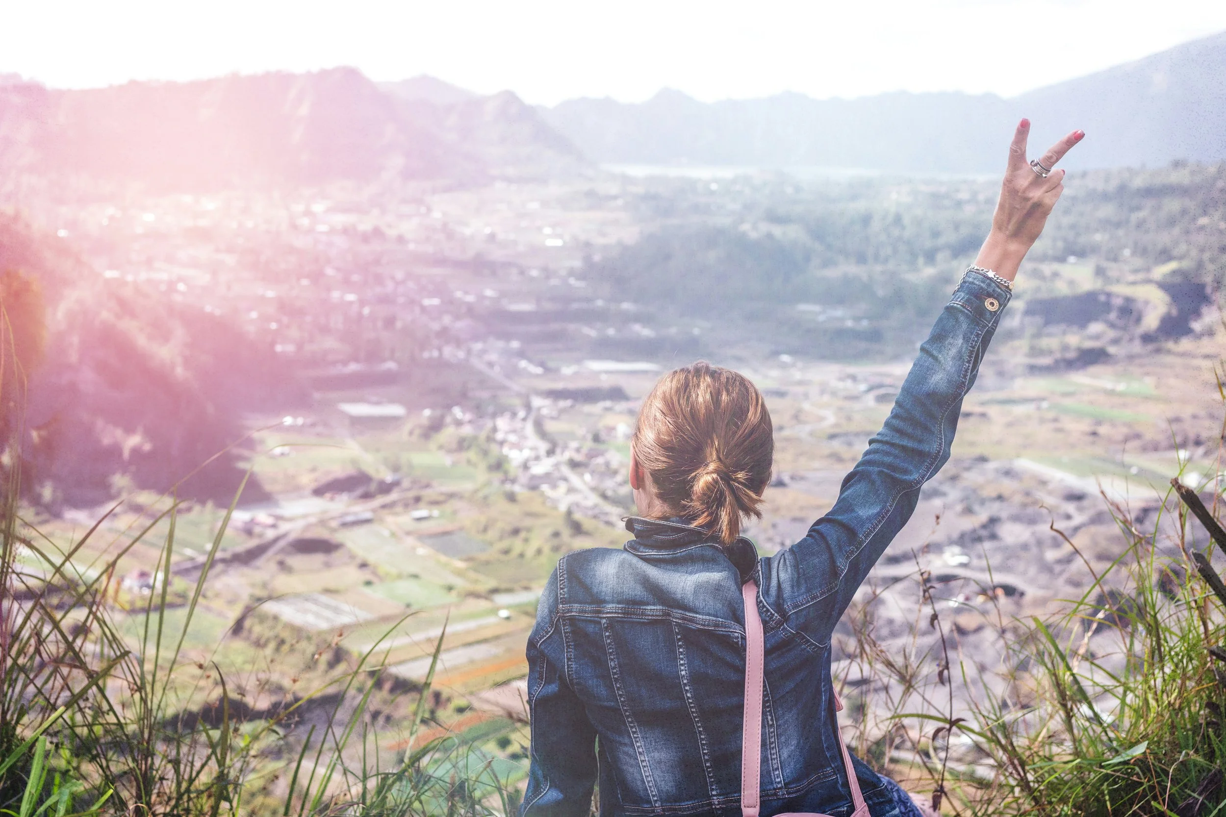 Women standing on a hill overlooking mountains and a town, making a peace sign.