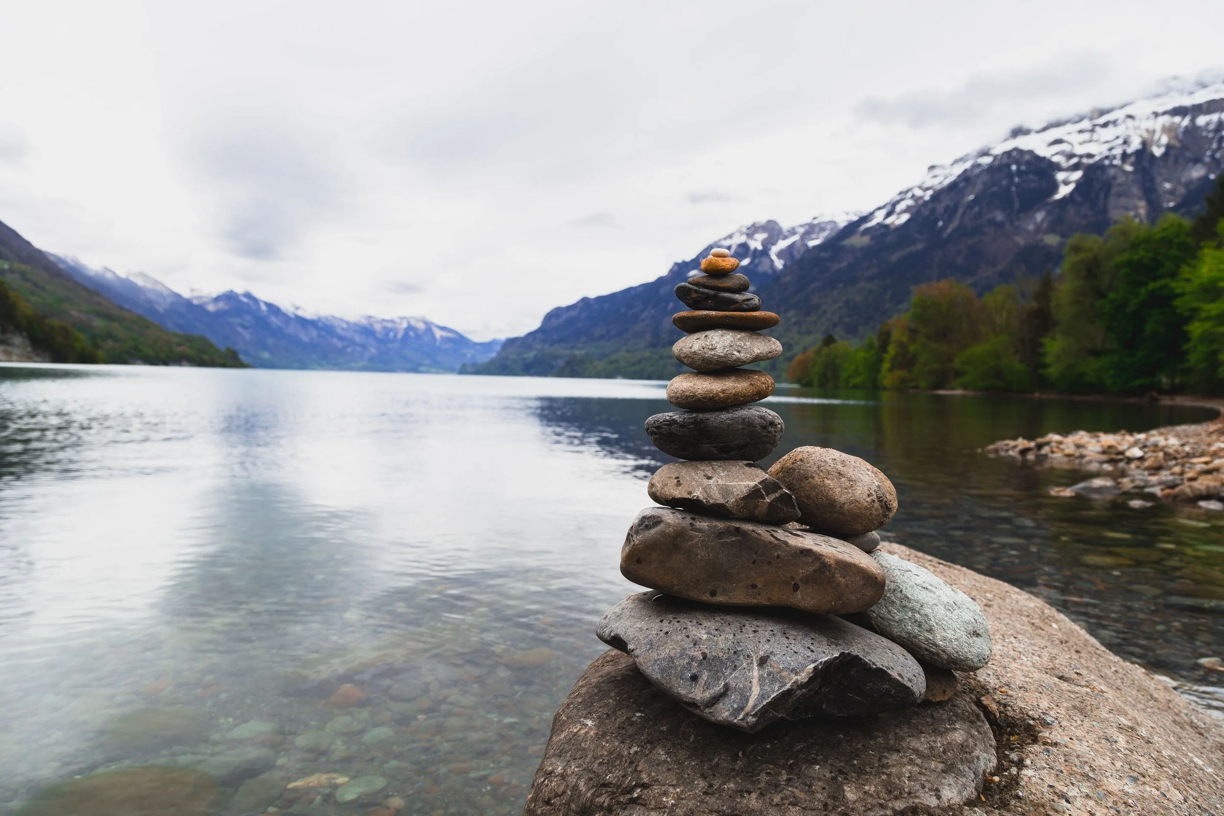 Cairn of stacked stones on a lakeshore with mountain and a cloudy sky in the background.