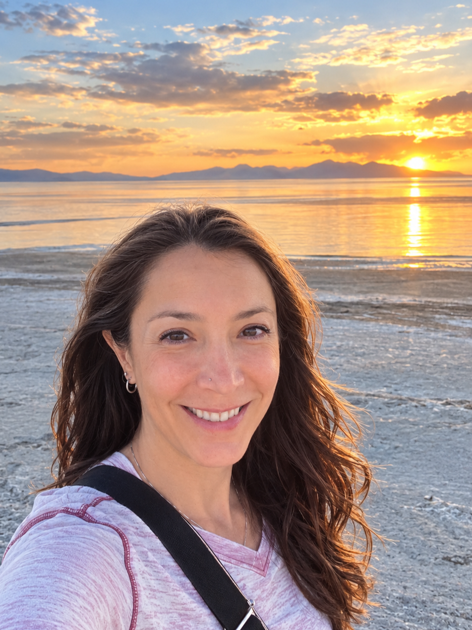 Emily Arden at the Great Salt Lake at sunset, with mountains and a colorful sky in the background.