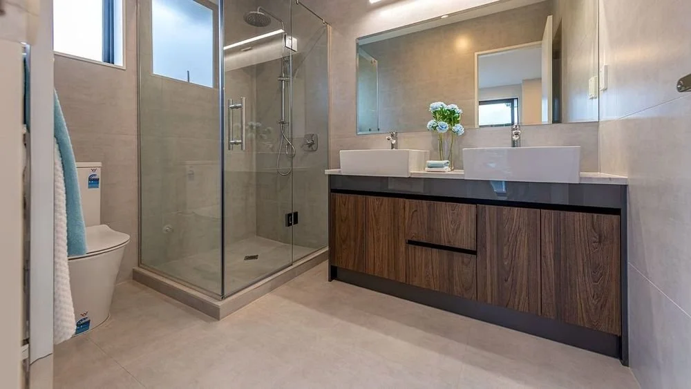 Modern bathroom with double vanity, large mirror, glass-enclosed shower, and a toilet, decorated with fresh flowers.