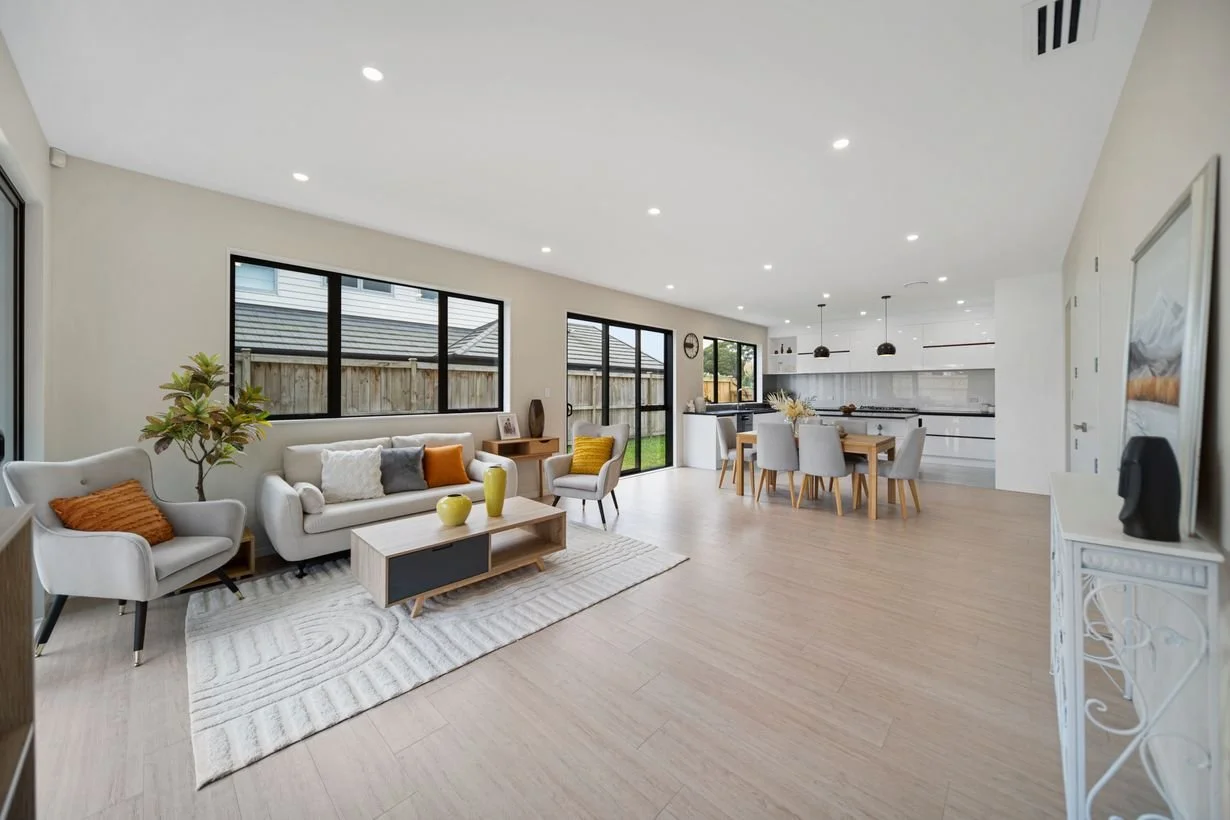 Bright open-concept living room and kitchen with modern furniture, white walls, hardwood flooring, large windows, and minimal decor.