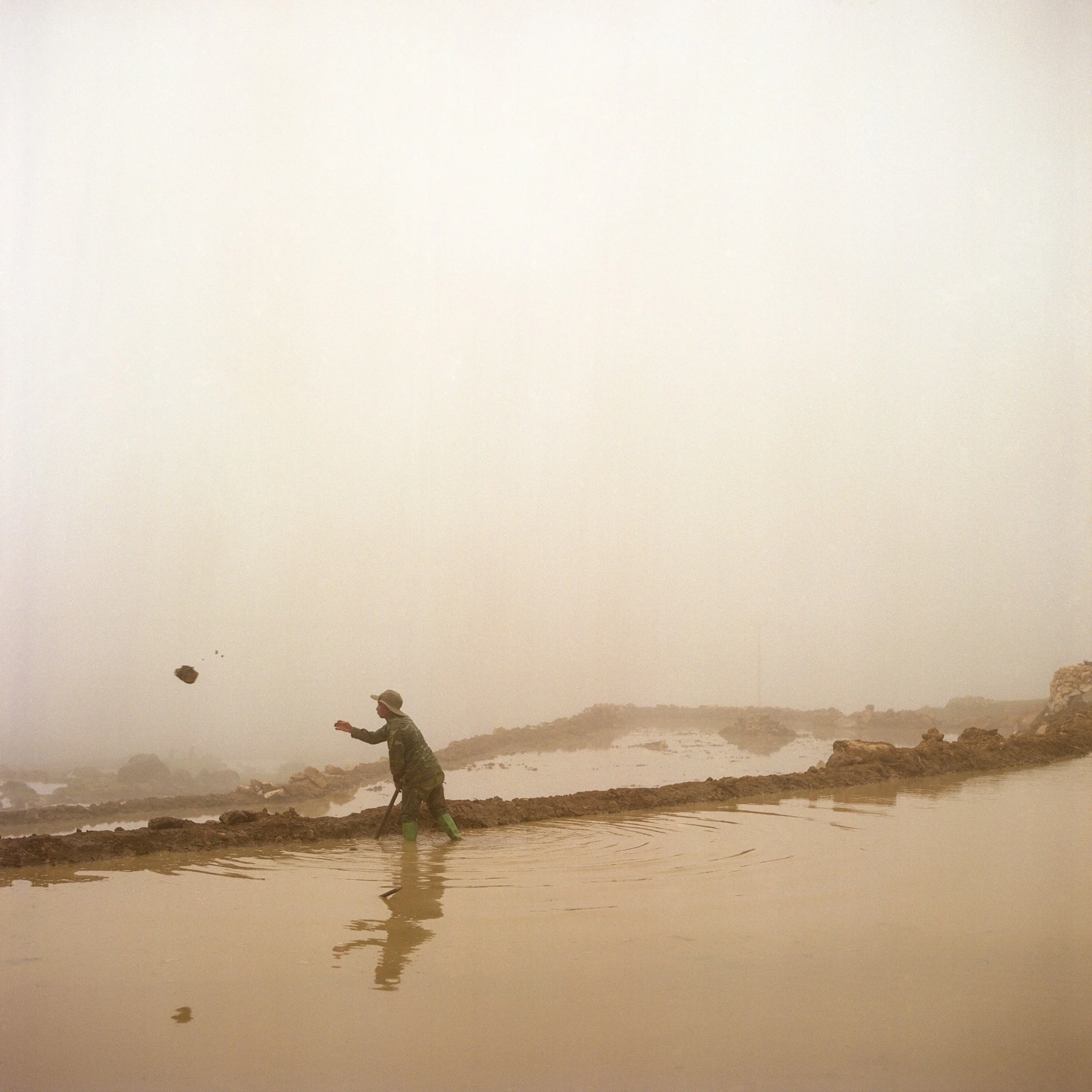 	
In Sa Pa, Vietnam, A person standing in water near a muddy bank during a sandstorm, throwing a rock into the air.