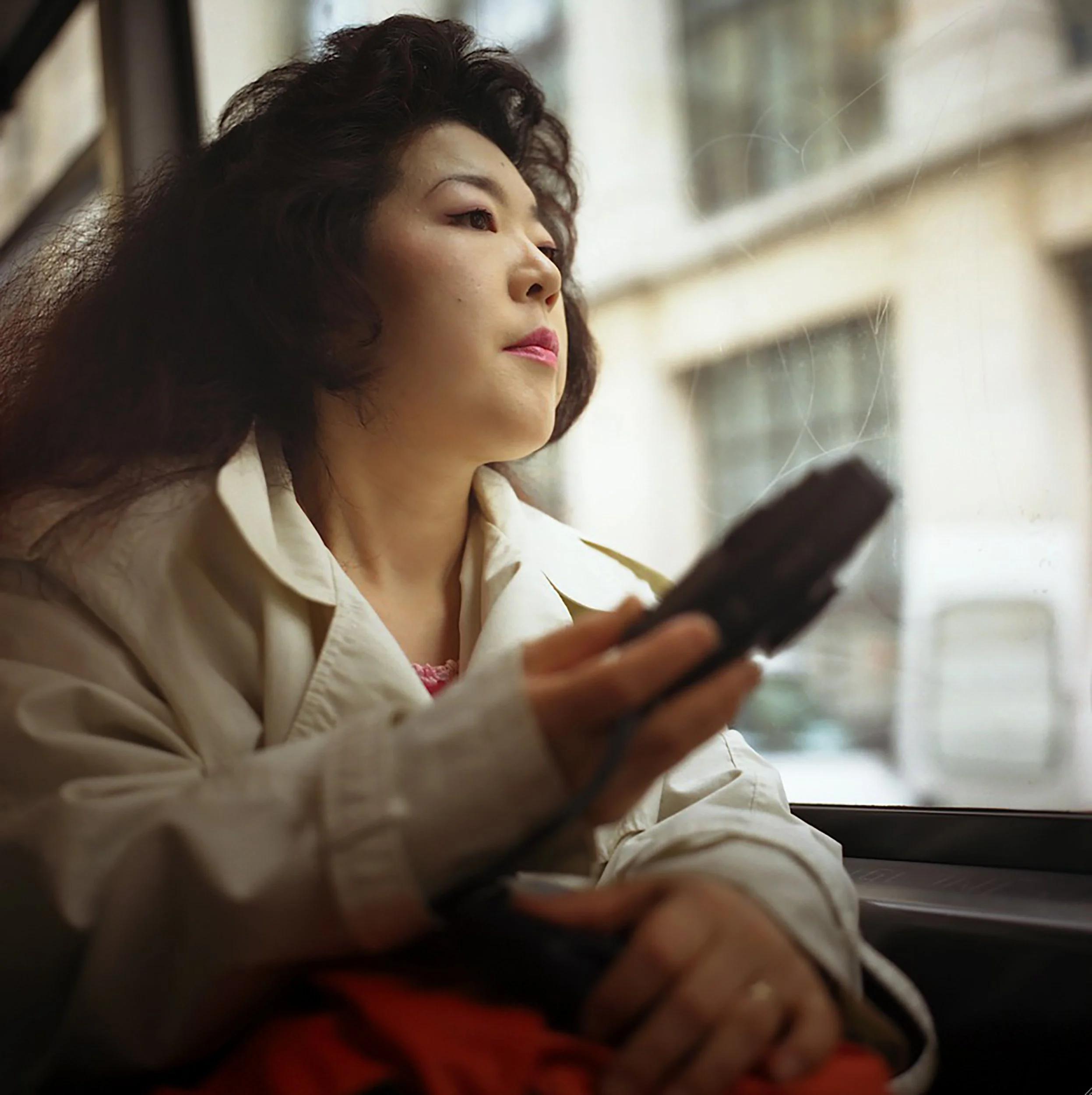In Paris bus, Close-up of a woman with curly hair looking out a window, with blurred details in the foreground.