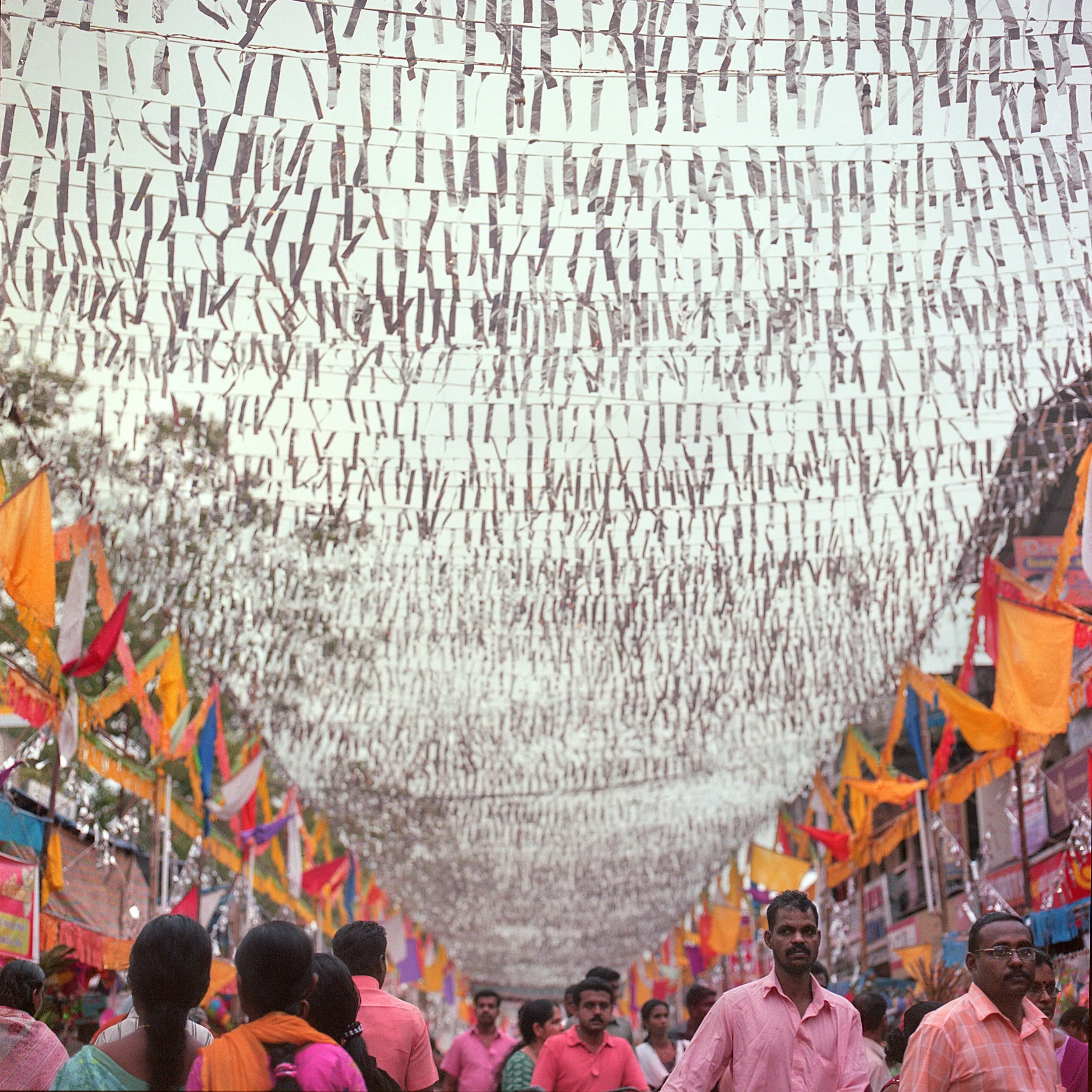 In Alleppey, Kerala, India, People walking under a canopy of hanging paper decorations and colorful flags at an outdoor event in India.
