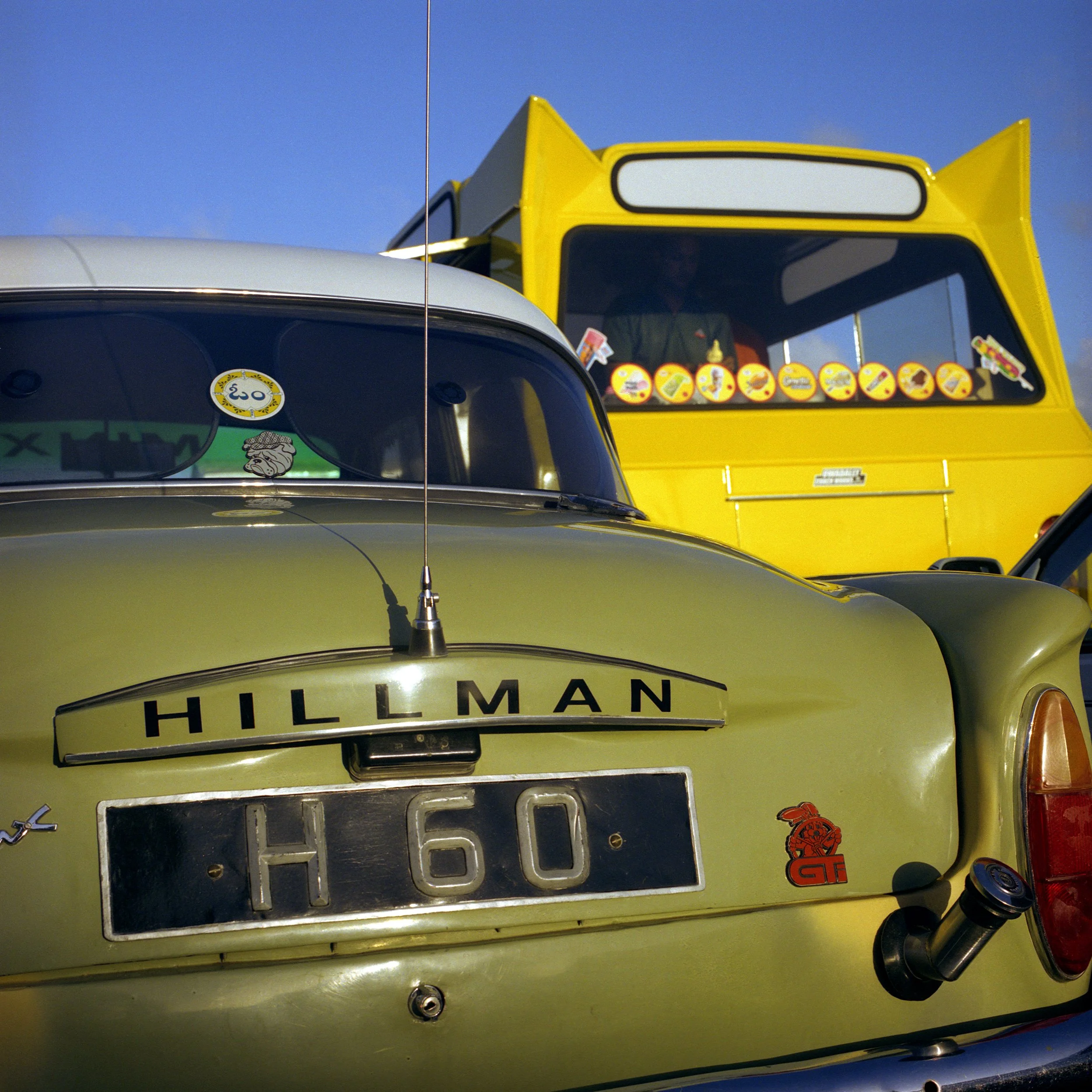 In Mauritius, Gris-Gris-SOuillac, Close-up of a vintage yellow and gray Hillman car parked outdoors with a bright blue sky in the background. The car has a sticker on the rear window and features a distinctive badge on the rear.