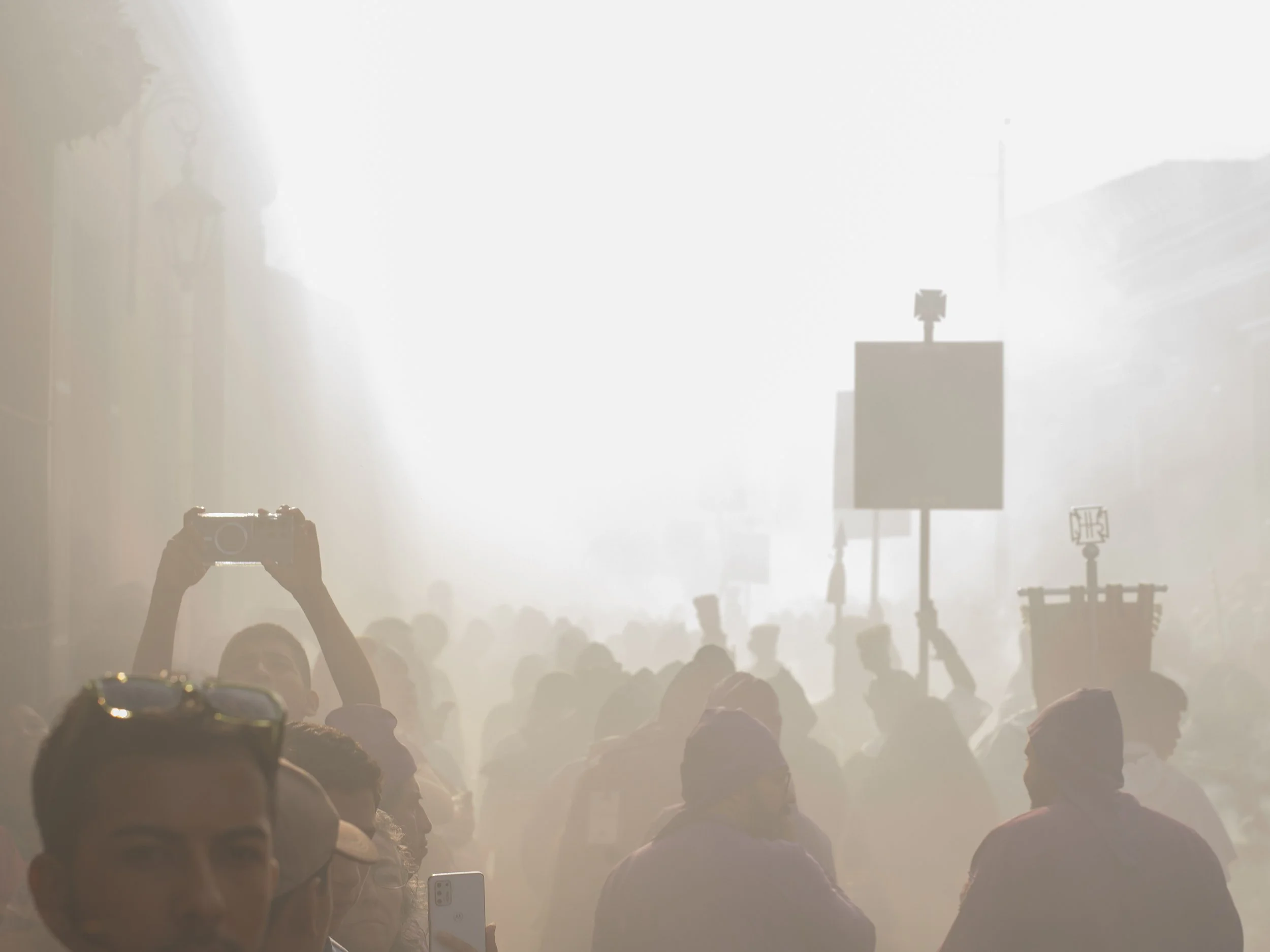In Antigua, Guatemala, Alfombras, Crowd of people in a foggy, sunlit street, some holding signs and taking photos. Catholic procession
