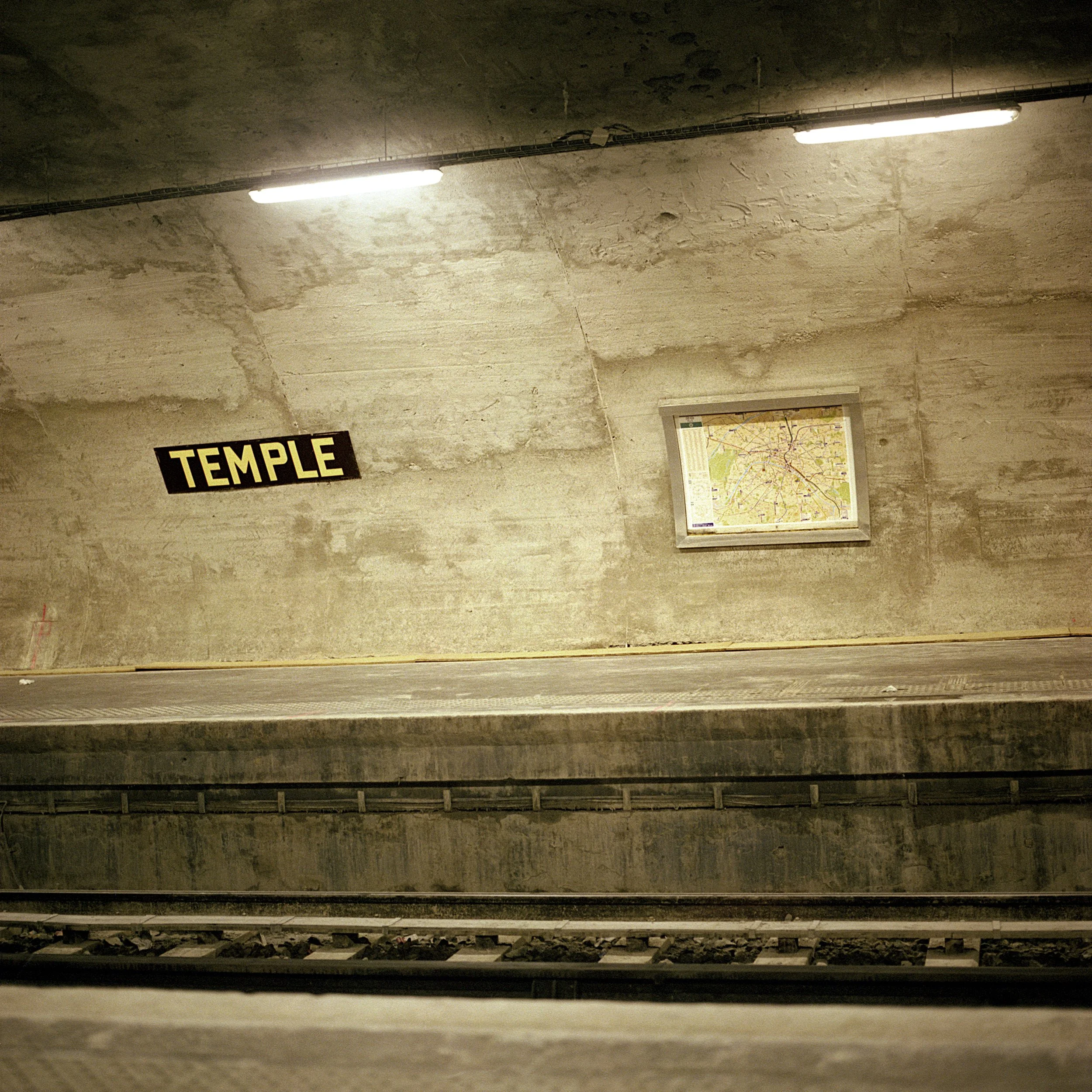 A subway station platform with a sign labeled "TEMPLLE" and an illuminated map of the subway system on the wall.