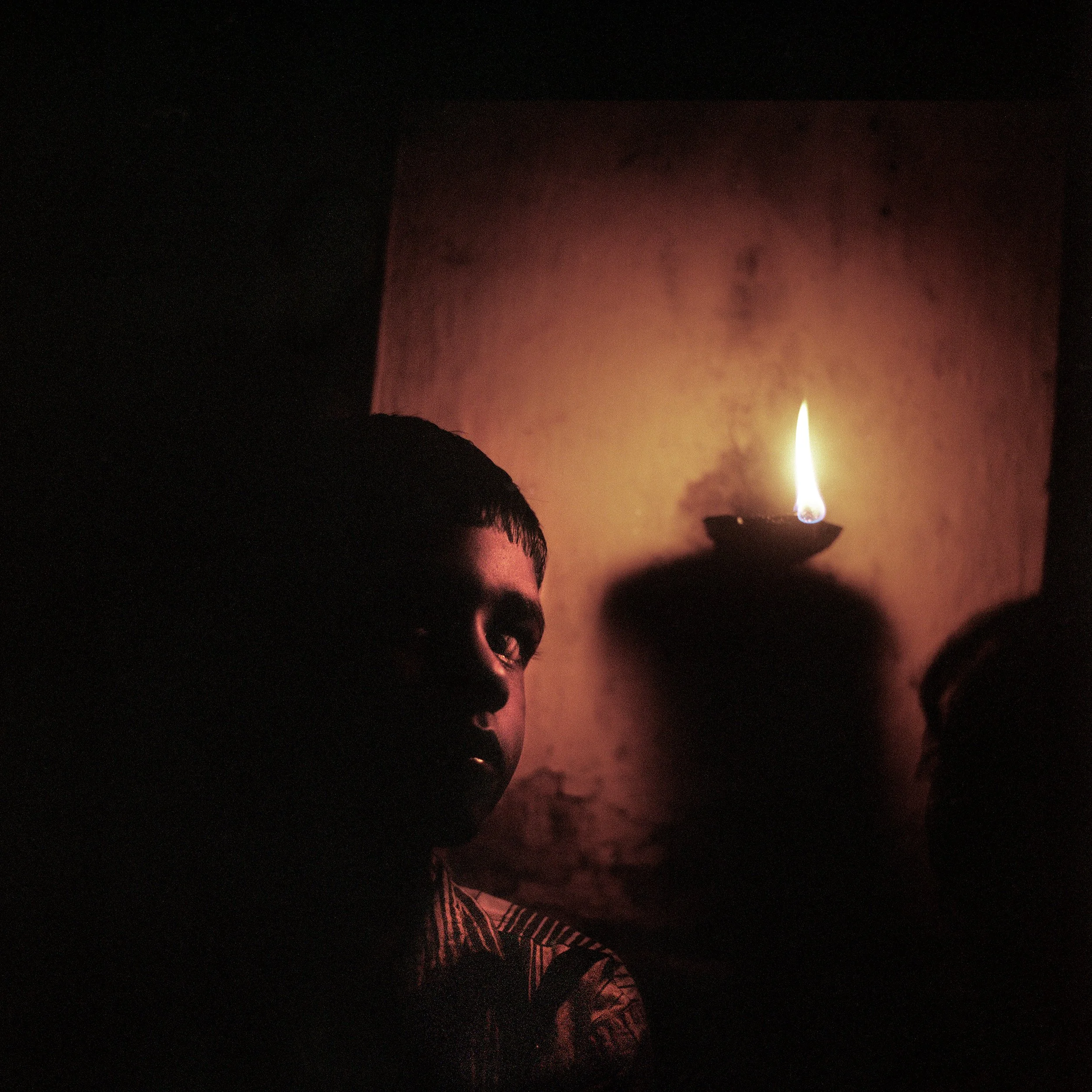 In Kerala backwaters, India, A young boy, silhouetted against a dark background with a small flame or light source on the wall. dipawali