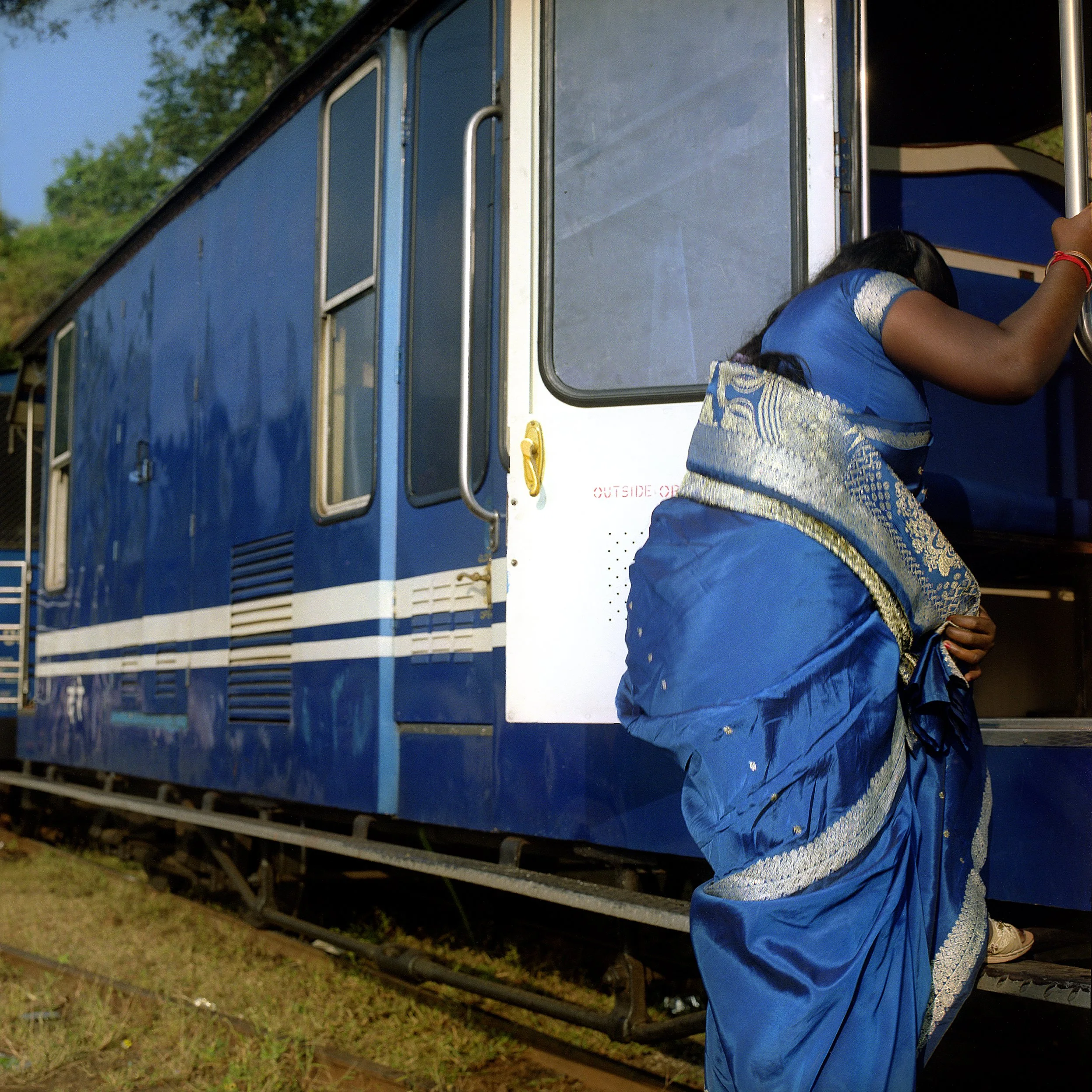 Woman in a blue sari entering a blue train or tram