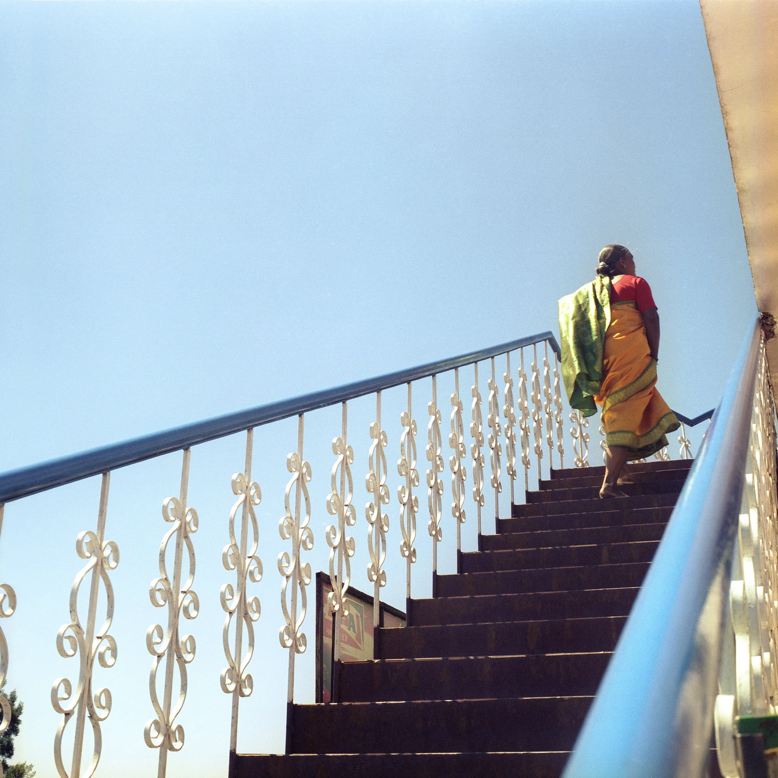 Woman ascending staircase with intricate white railing on a clear day.