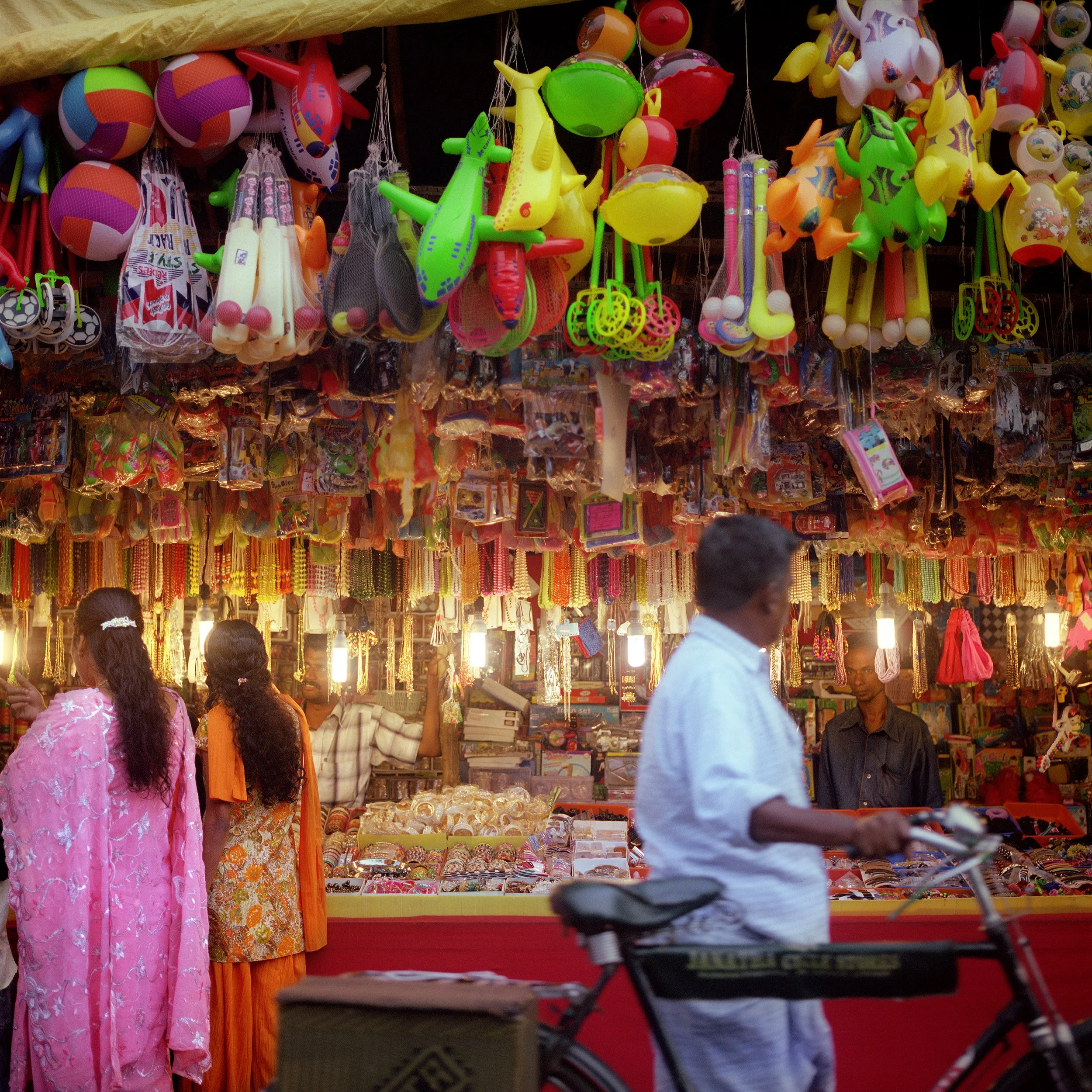 In Kerala, India, Alleppey, Colorful toys hanging at a market stall, with people browsing below.
