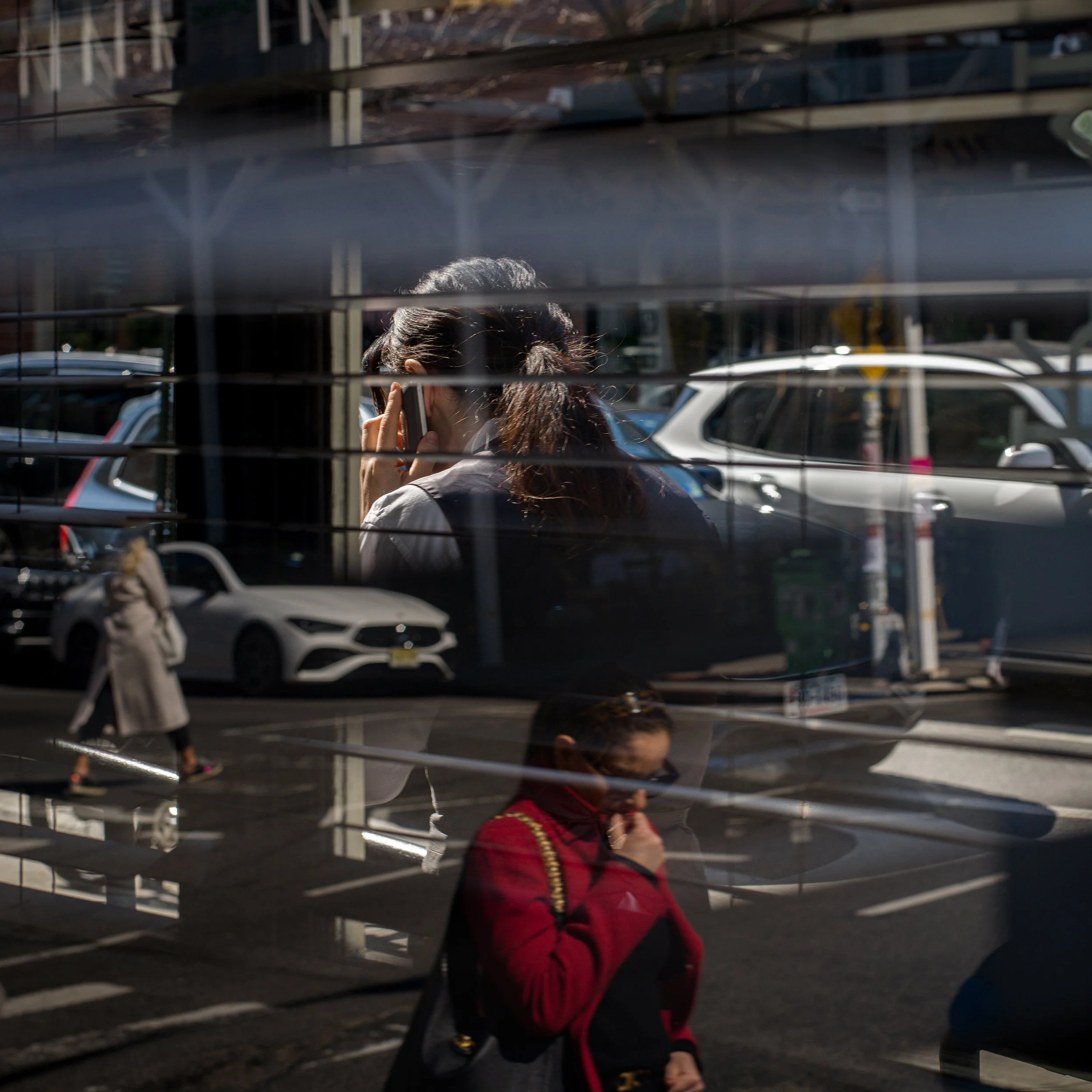 In New York Manhattan, Reflected image of two women walking on the street, one talking on her phone, seen through window blinds on a sunny day.