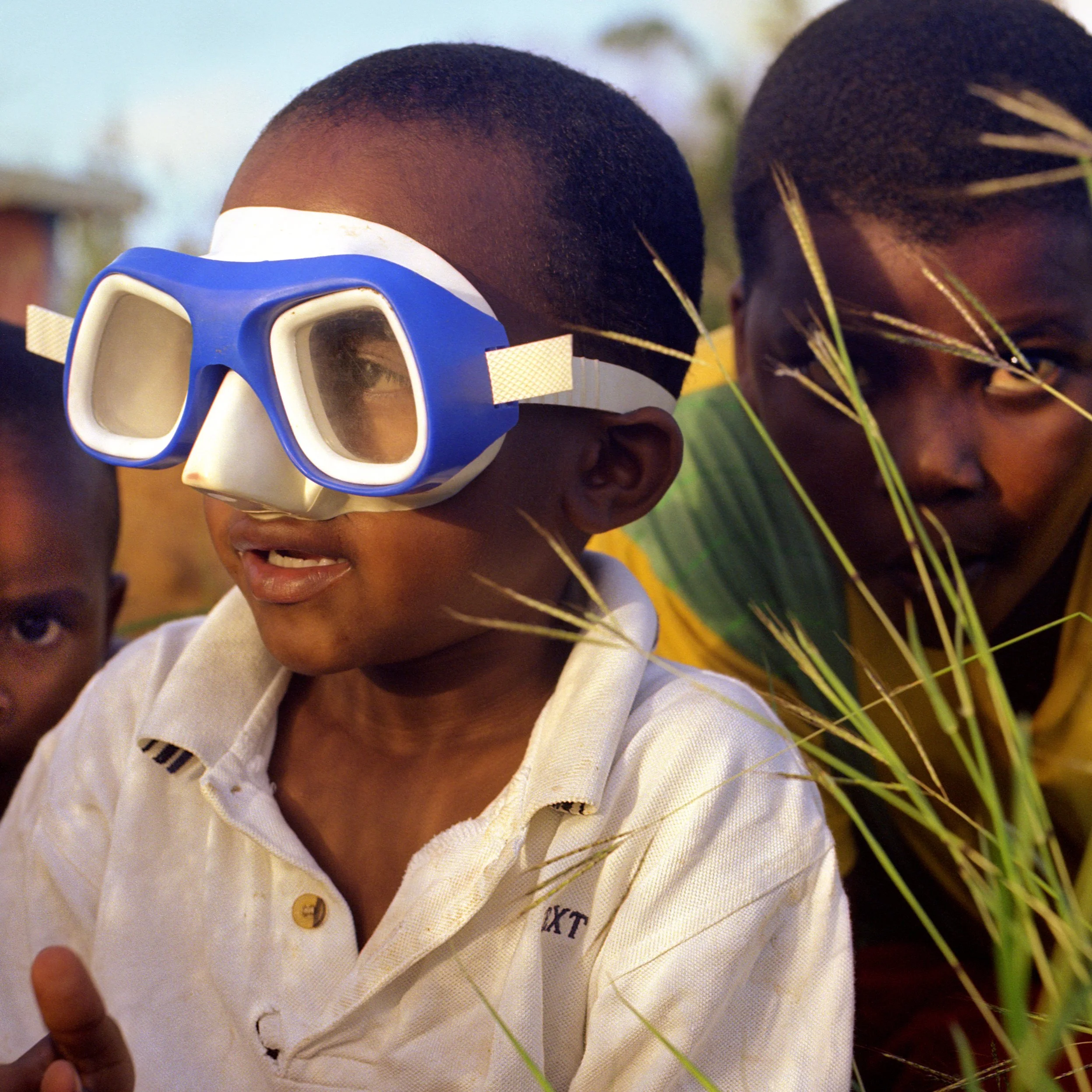 In Rodrigues Island, Mauritius, Young boy wearing snorkel goggles, outdoors with tall grass, accompanied by two other children, one with braided hair, in a natural setting.