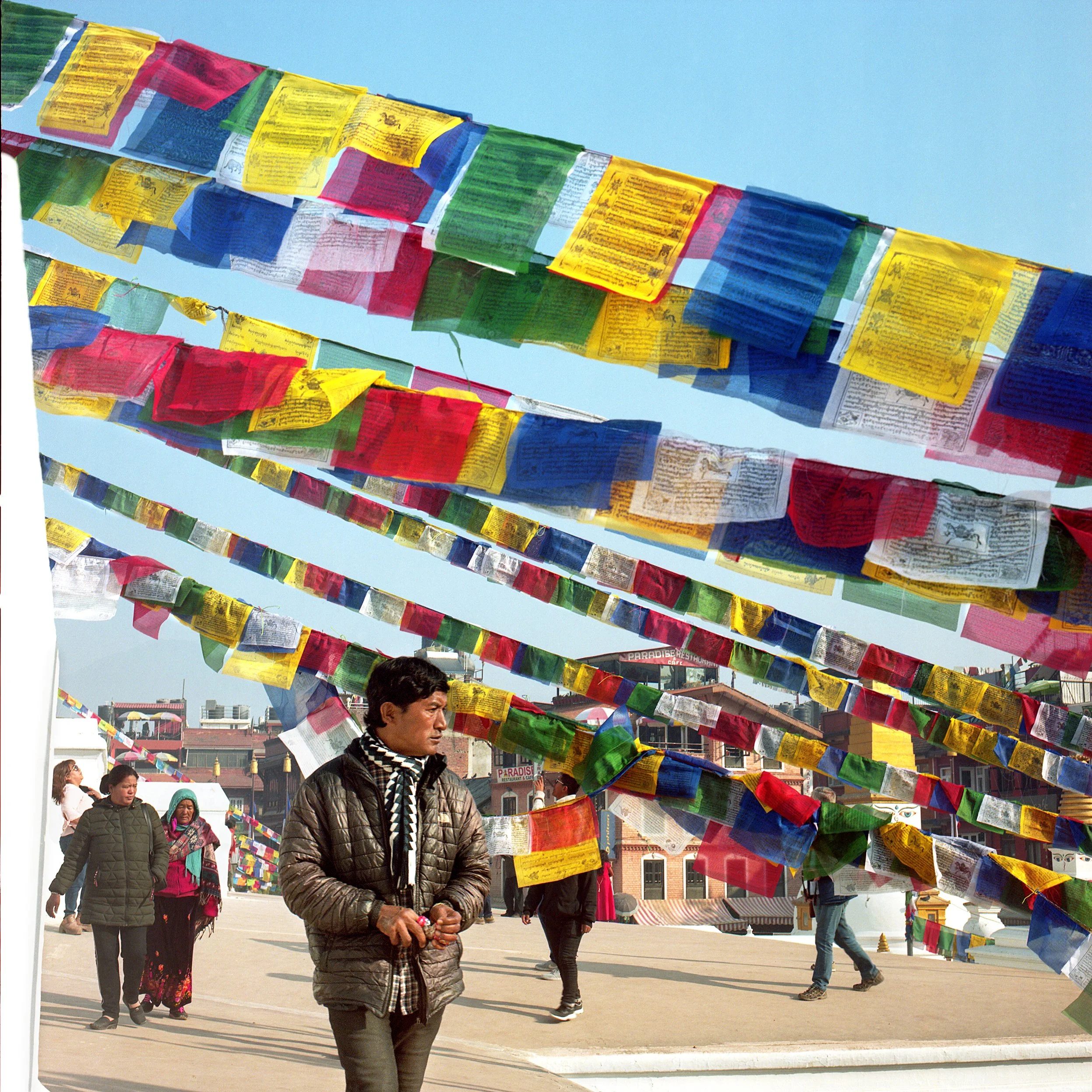 In Kathmandu People walking under colorful prayer flags hanging in the sky during daytime in a busy outdoor area.