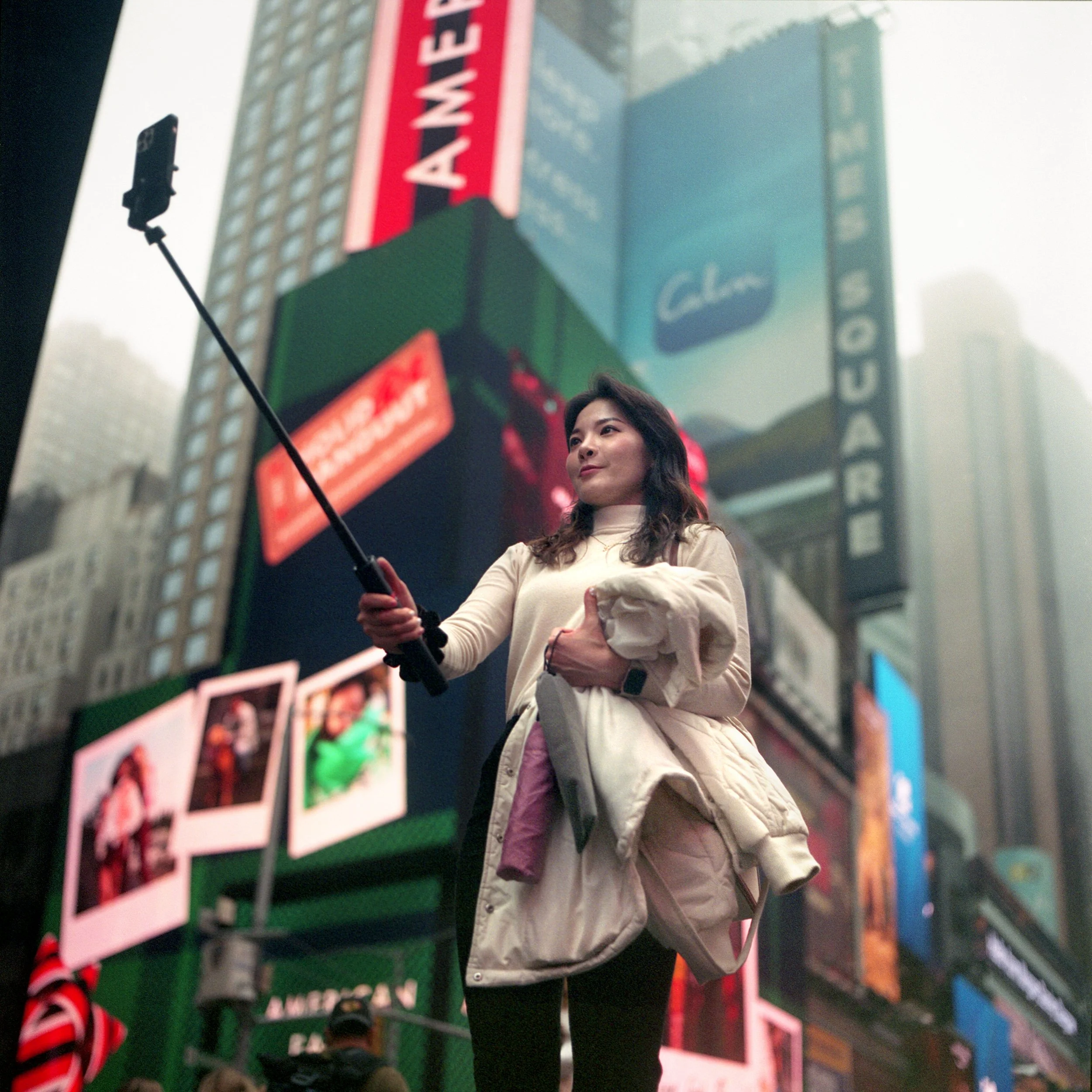 In New York Manhattan, A woman takes a selfie with a selfie stick in Times Square, New York City, surrounded by bright electronic billboards and advertisements.