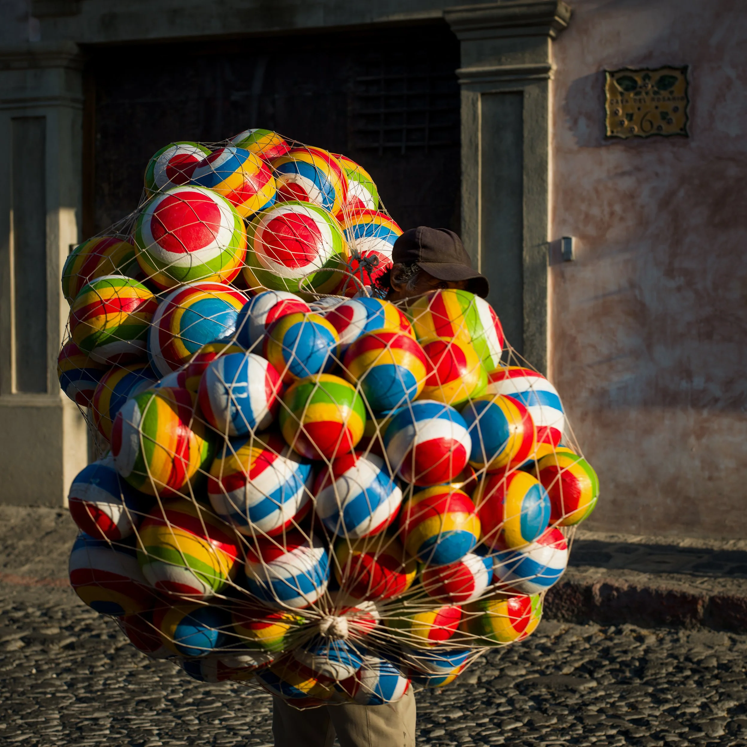 In Antigua, Guatemala, a Person carrying a large net filled with colorful beach balls on a cobblestone street.