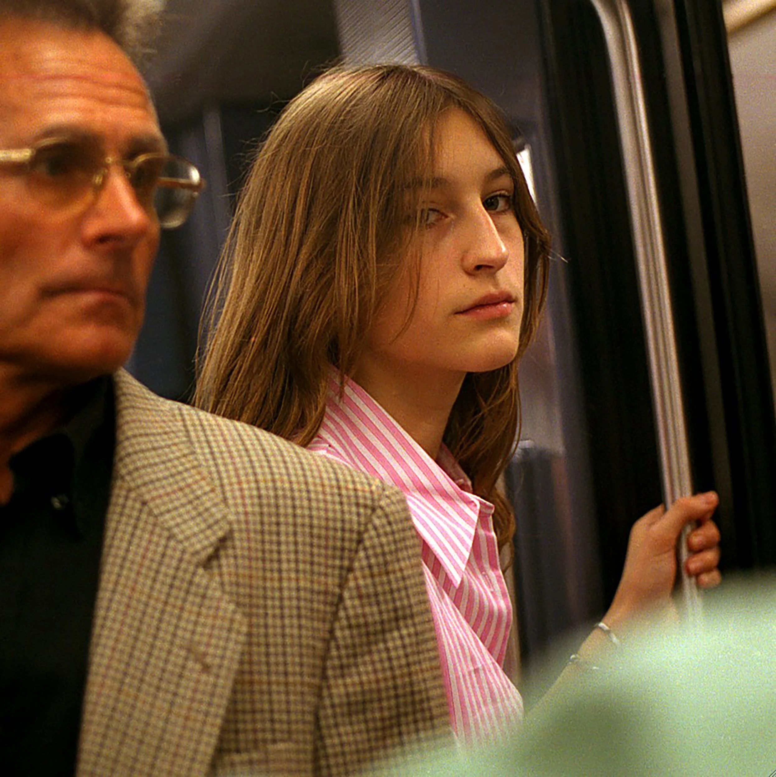 In Paris Subway, Close-up of two people on a subway, including a woman with long brown hair wearing a pink striped shirt, and a man with glasses, both appearing to be sitting near the window.