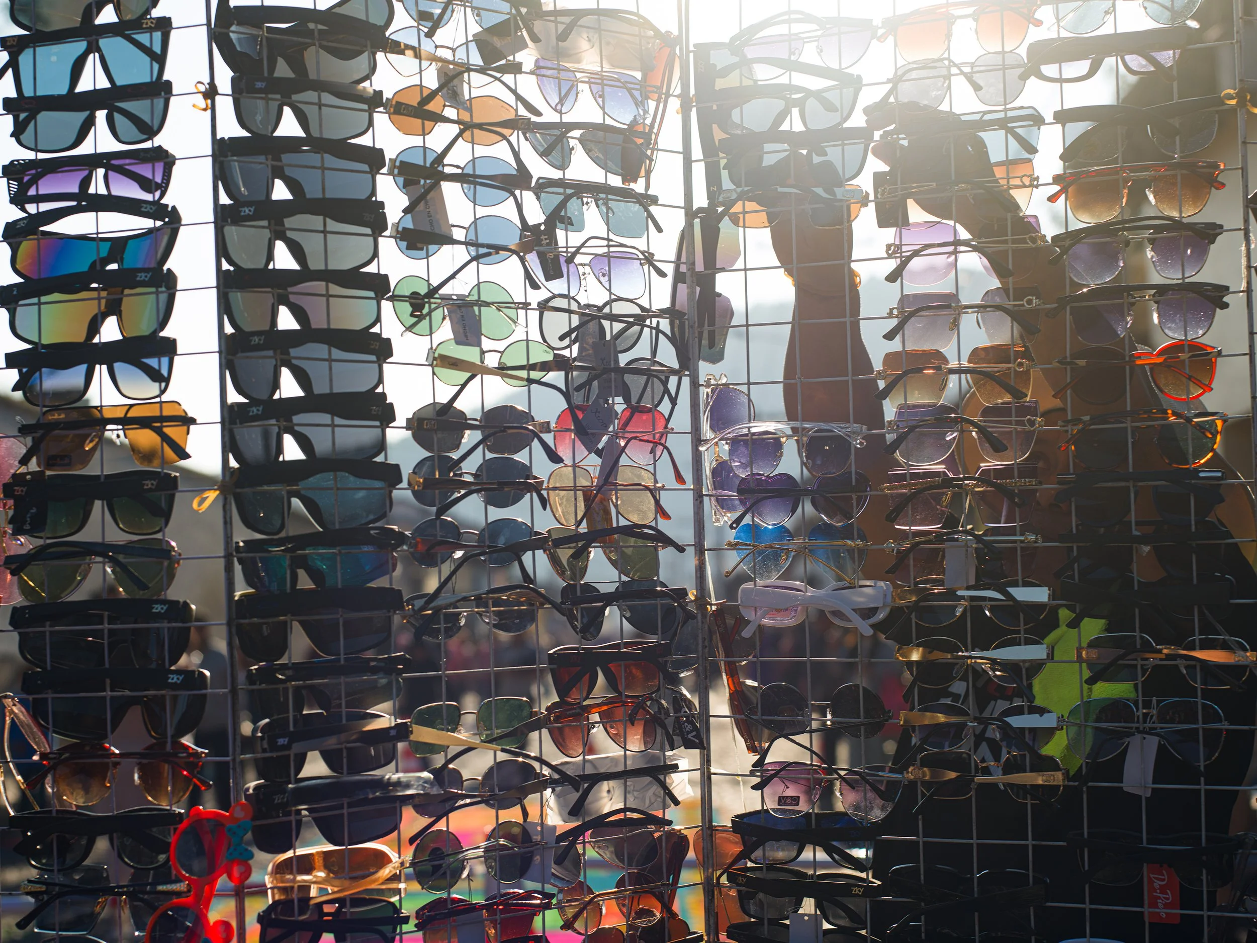 In Antigua, Guatemala, Alfombras, Display of sunglasses hanging on a wire grid at an outdoor market with sunlight shining through.