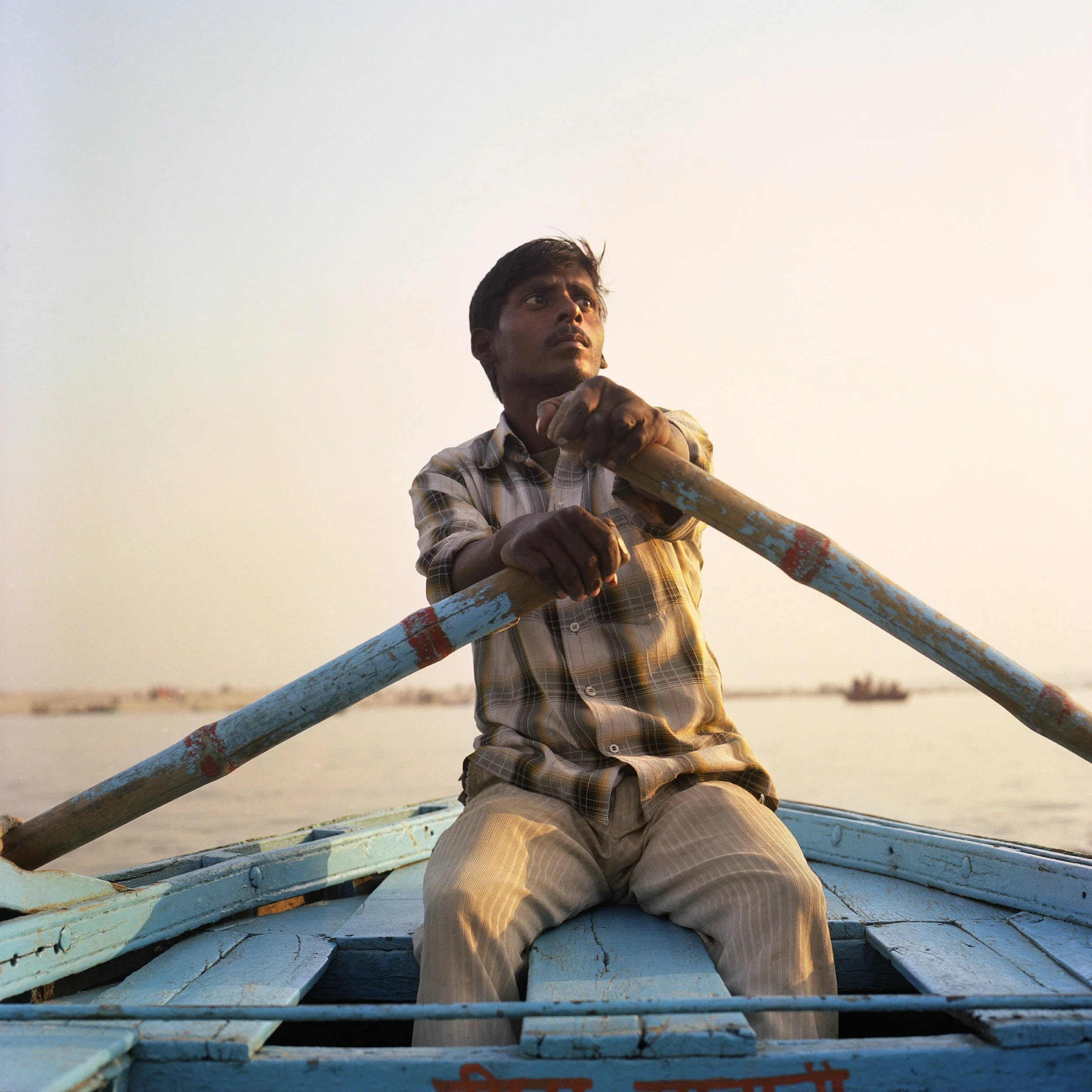 Man rowing a boat on a calm body of water during sunset.