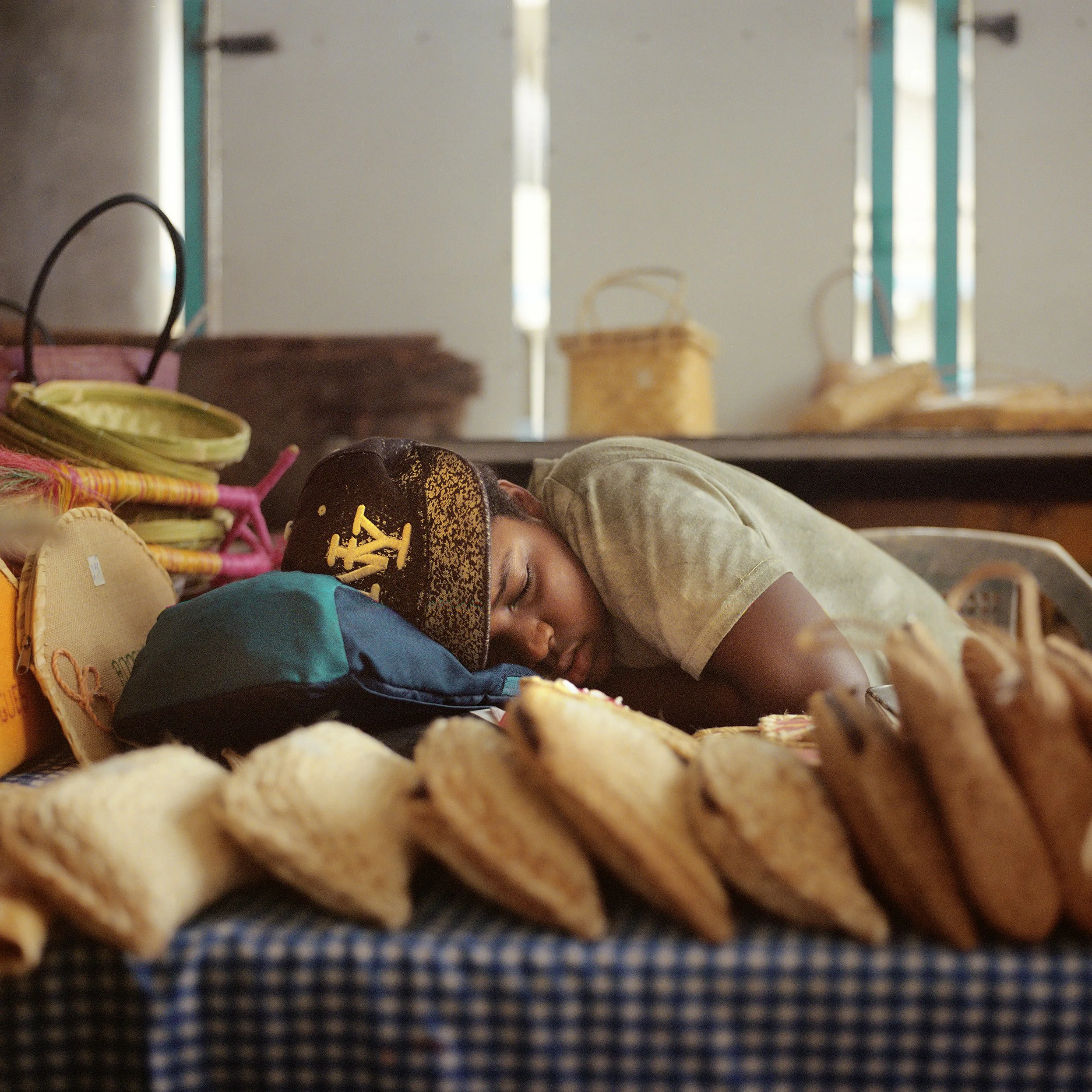 Person sleeping on a table with baked goods and bags around, in a bakery or shop setting.