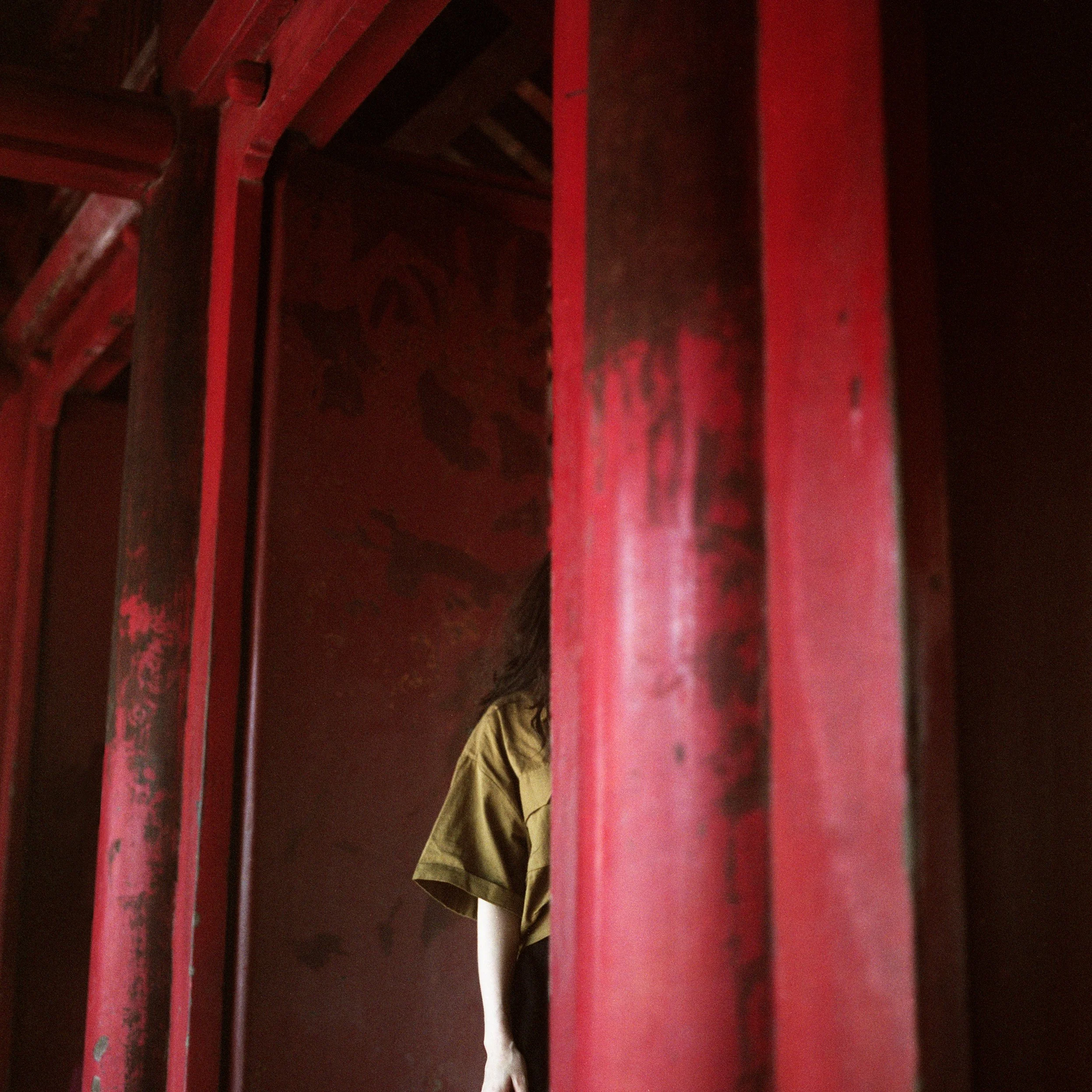 In Hanoi, Vietnam, A person in a yellow shirt leaning against a red wall with their head partially visible behind a red wooden post.