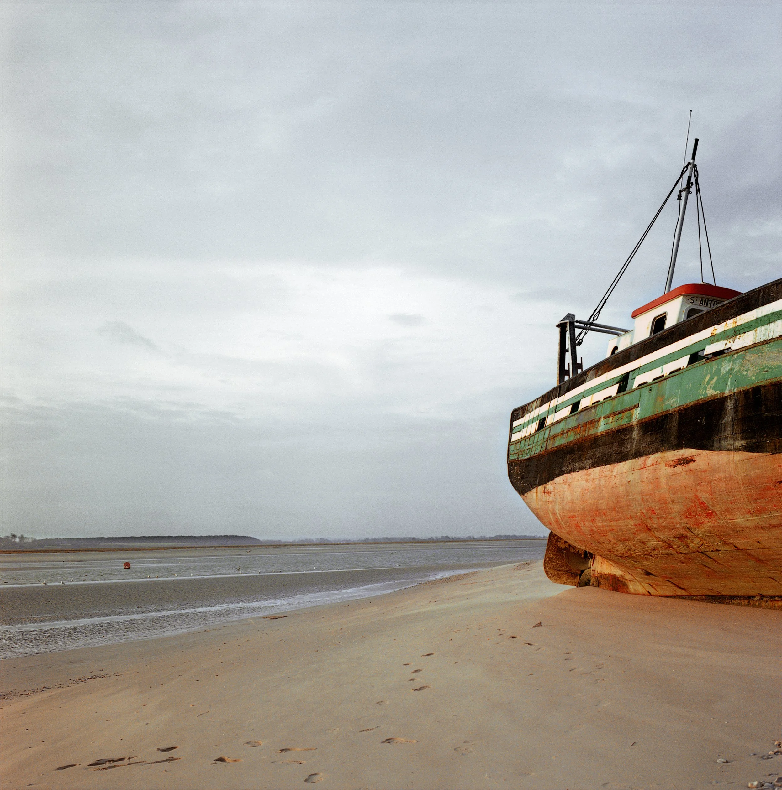 An old boat resting on the sandy beach under a cloudy sky.