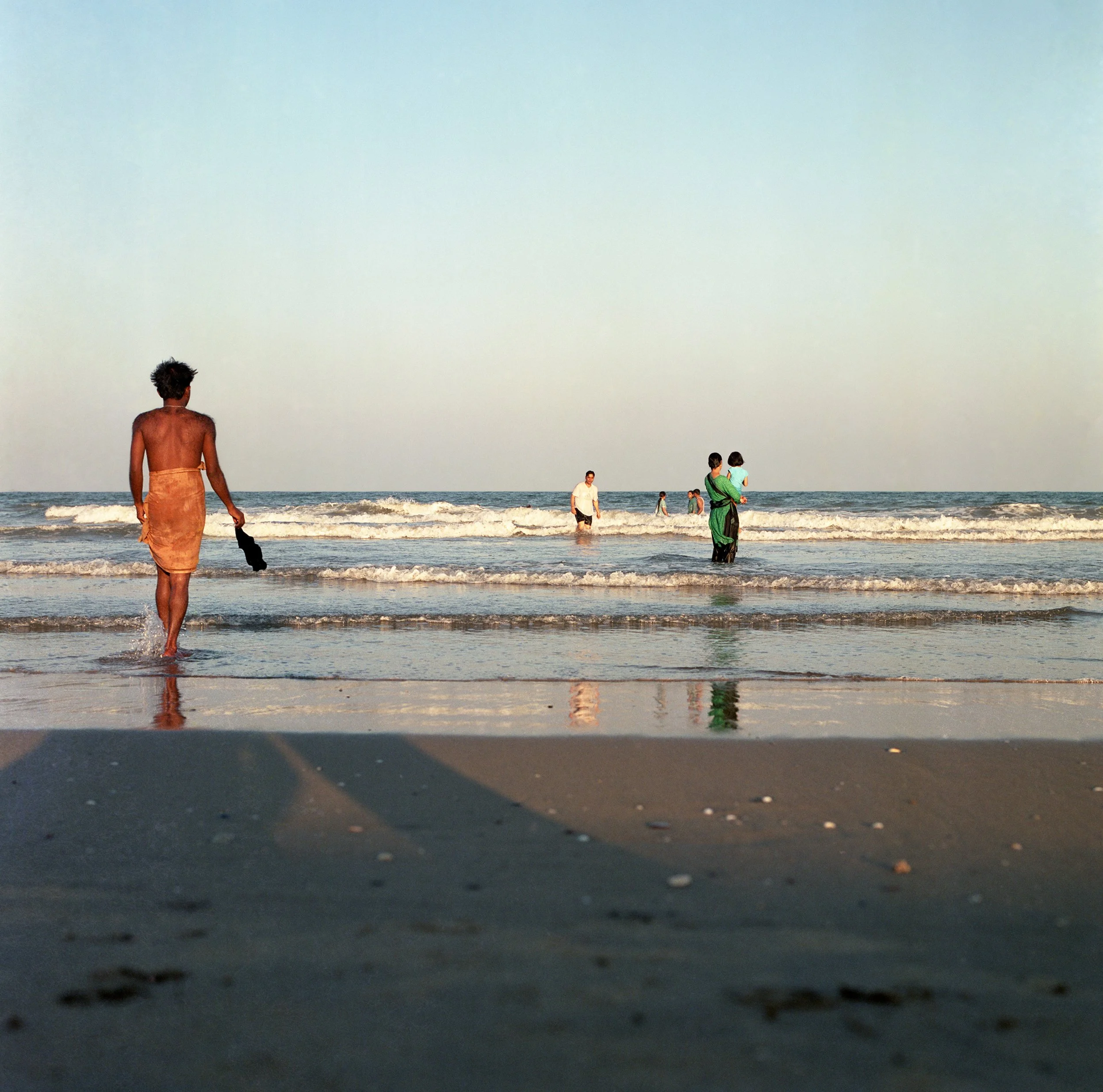 People enjoying a day at the beach with waves and clear sky in the background.