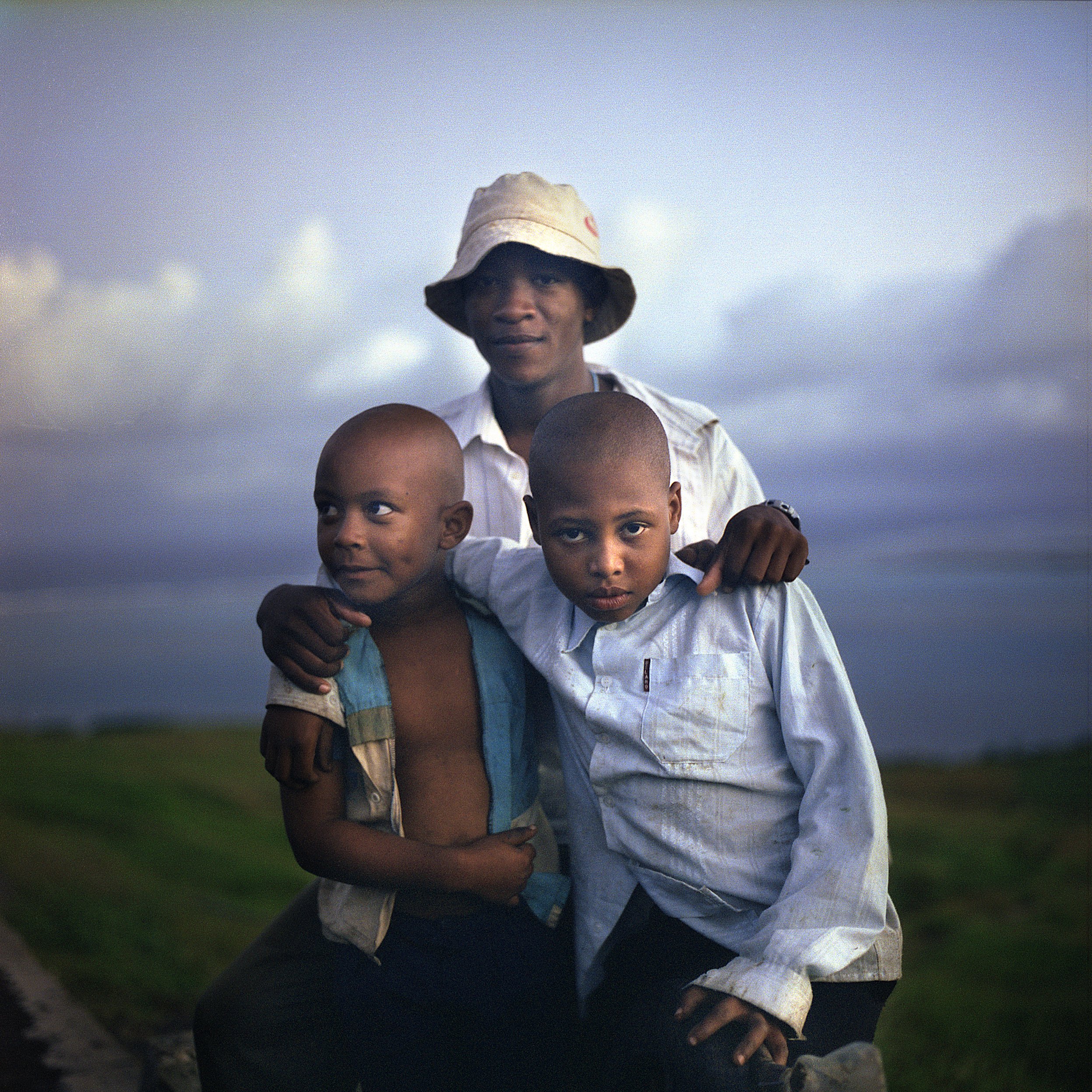 In Rodrigues island, Mauritius, outdoors with three children, The background shows an overcast sky and a grassy area.