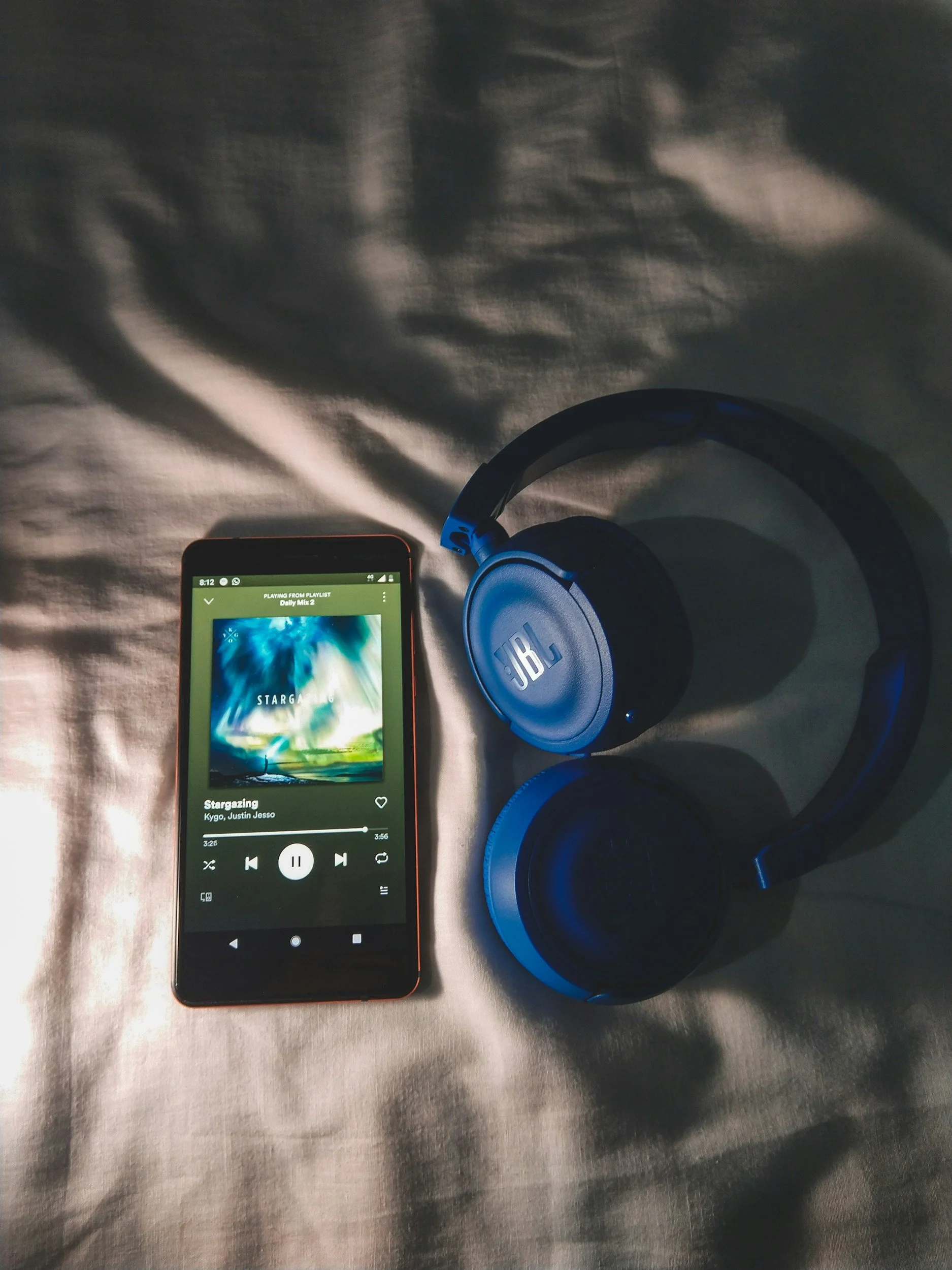 Smartphone playing music with a playlist titled 'Stargazing' and a pair of JBL over-ear headphones on a textured surface.