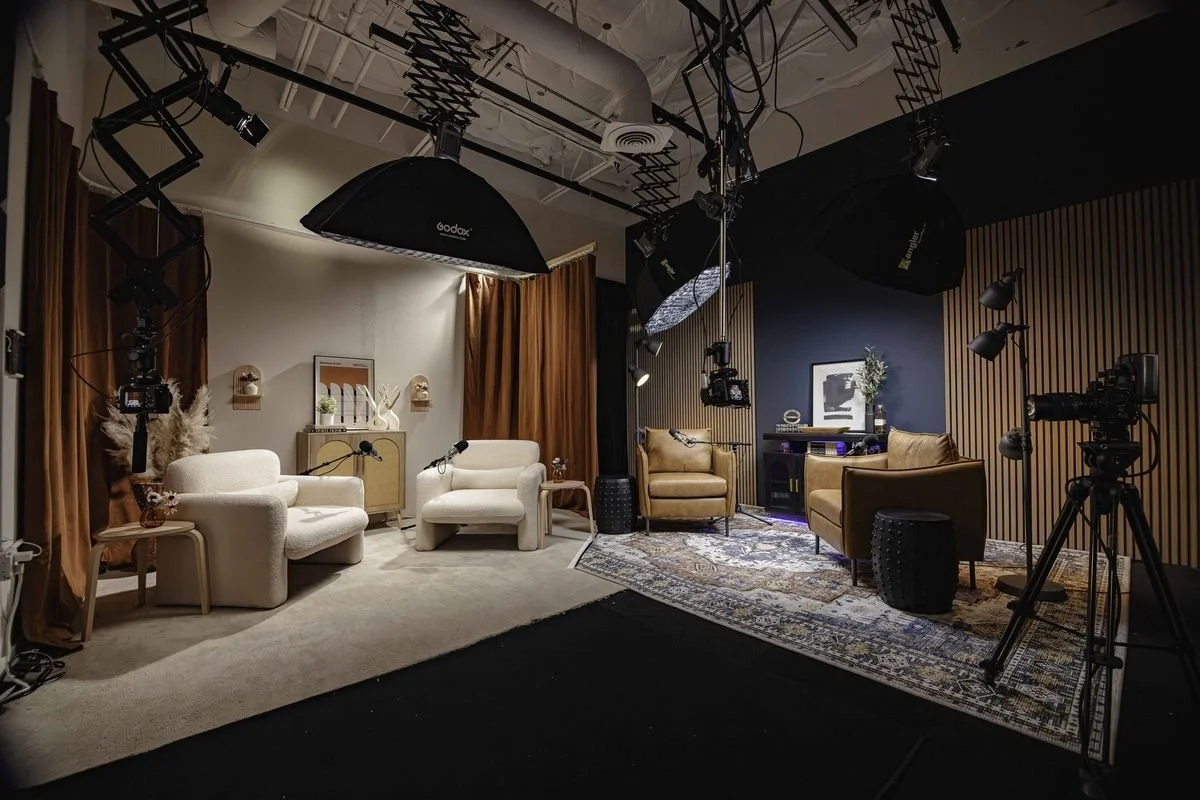 Photo of a cozy, stylish studio with two separate seating areas, professional lighting, and camera equipment, ready for filming or photoshoot.