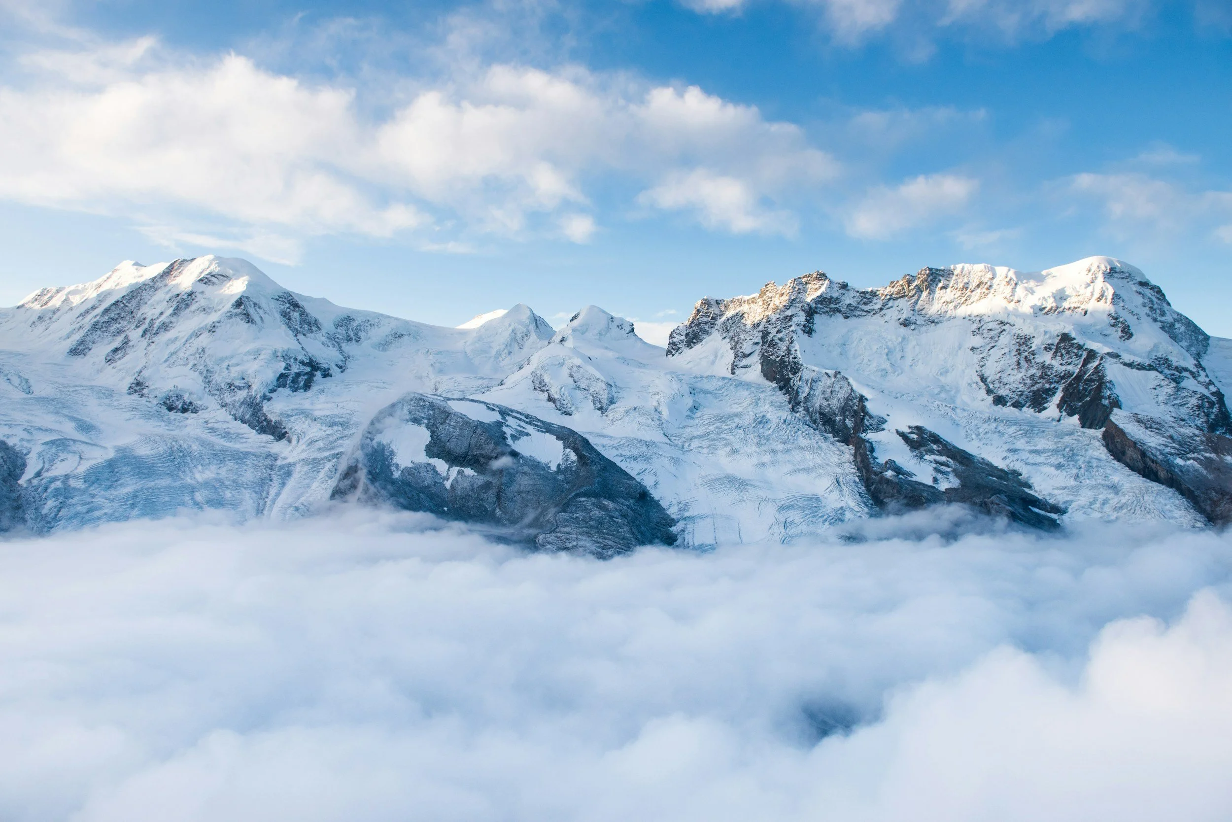 Schneebedeckte Berggipfel unter blauem Himmel mit einigen Wolken.