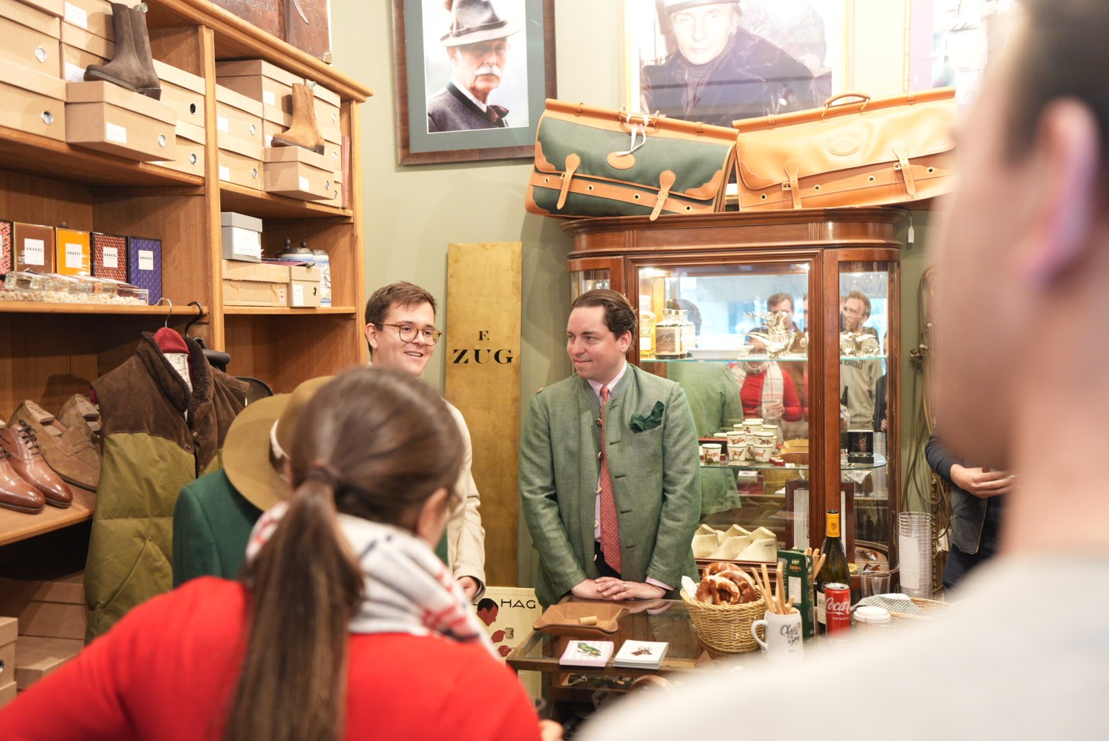 Menschen versammeln sich in einem Vintage-Laden, der mit Leder- und Schuhartikeln dekoriert ist, während zwei Männer hinter der Theke miteinander sprechen, umgeben von weiteren Gästen.