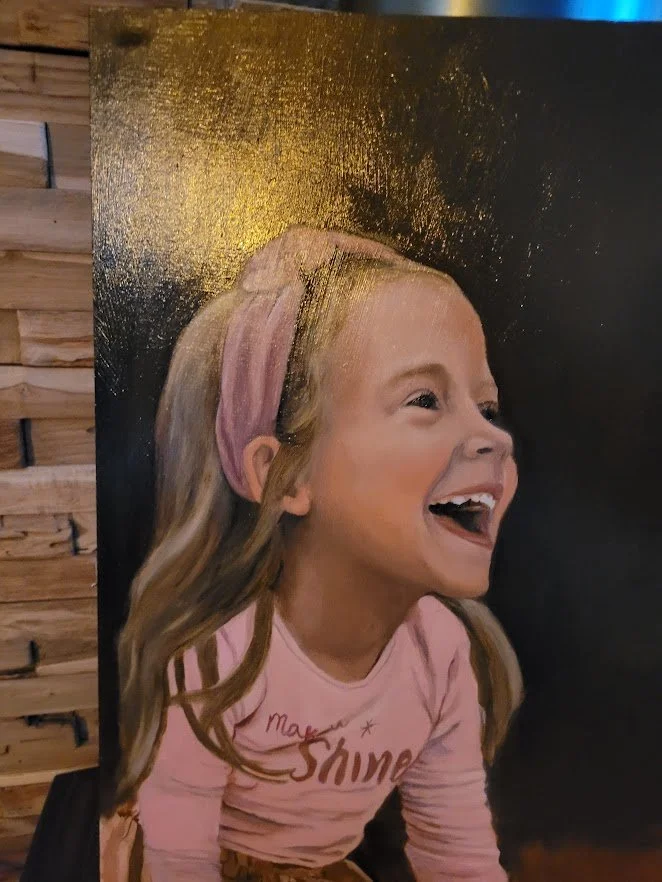 Een schilderij van een lachend meisje met lang haar, een roze haarband en een roze shirt met de woorden "Make Shine".