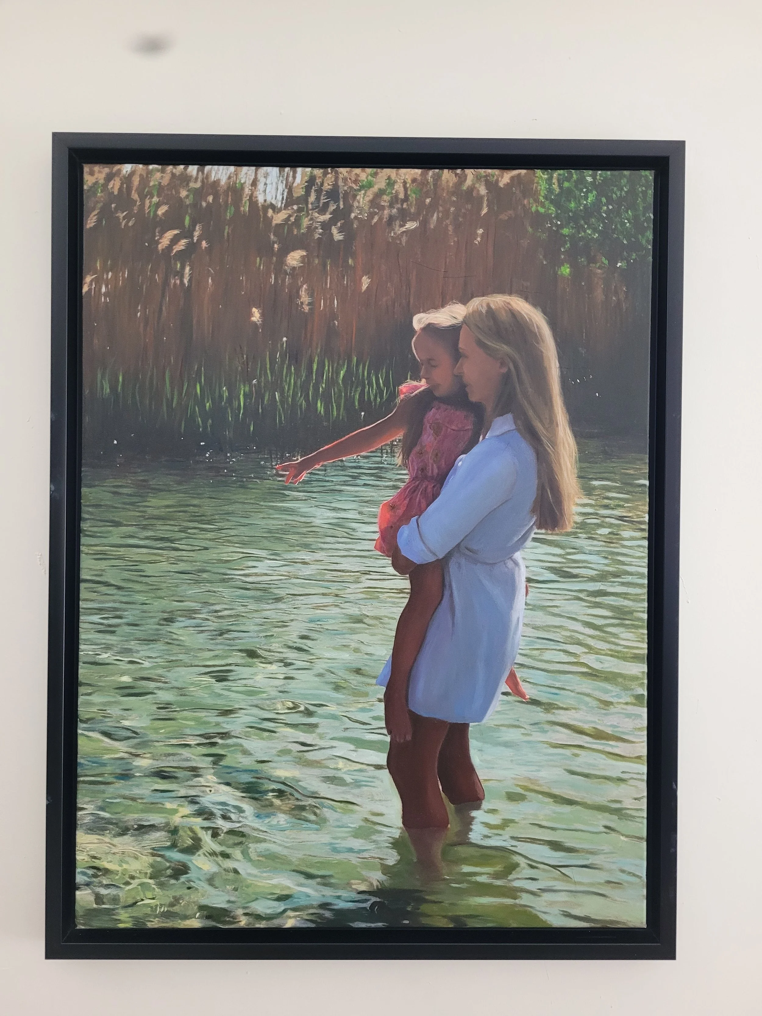 Twee meisjes staan in het water met een natuurlijke achtergrond, de ene houdt de andere vast terwijl ze zwijgend naar de horizon kijken.