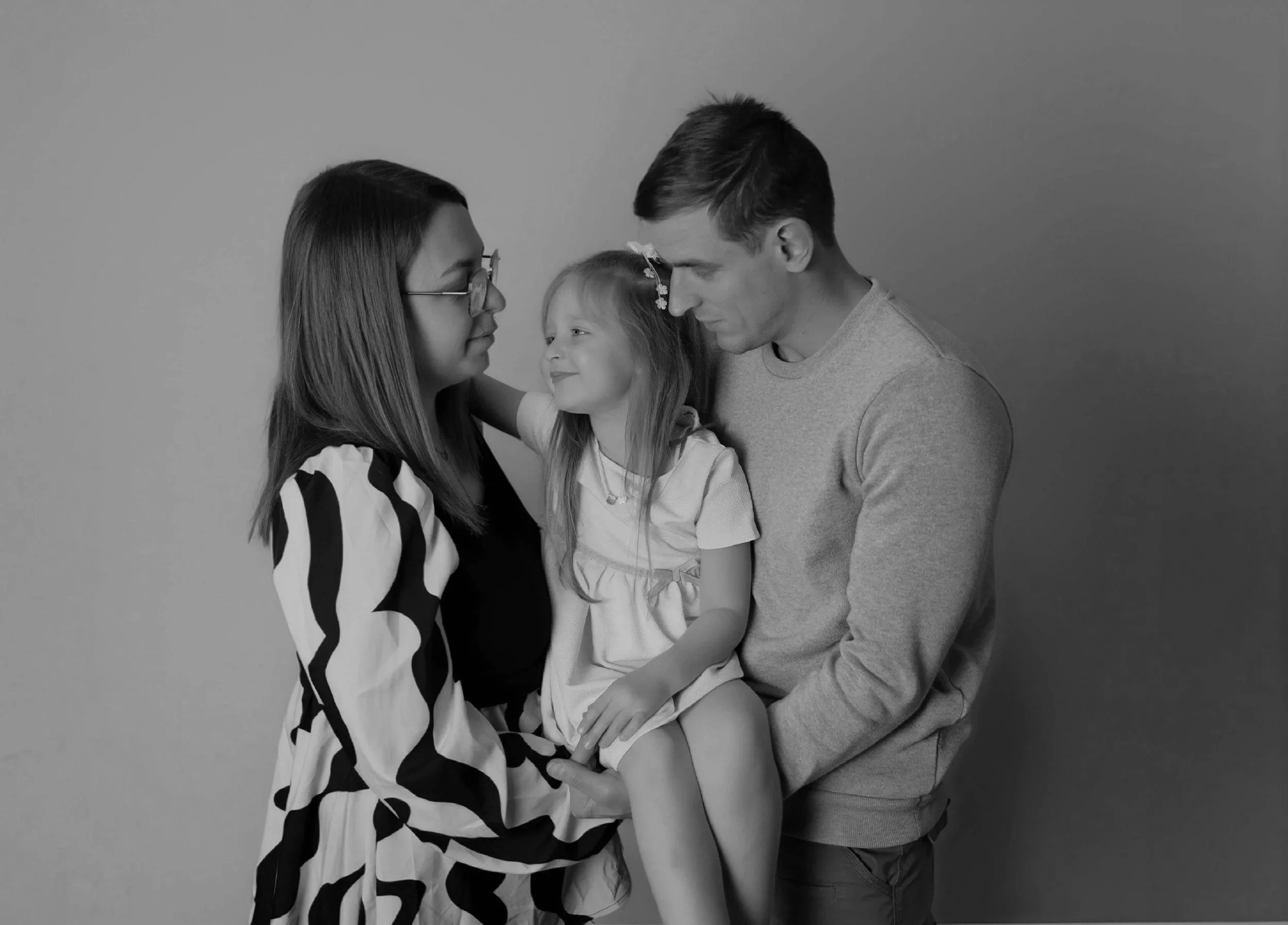 Une famille composee d'une femme, d'un homme et d'une jeune fille pose ensemble, on voit leur visage en premier plan, dans une ambiance tendre et affectueuse.