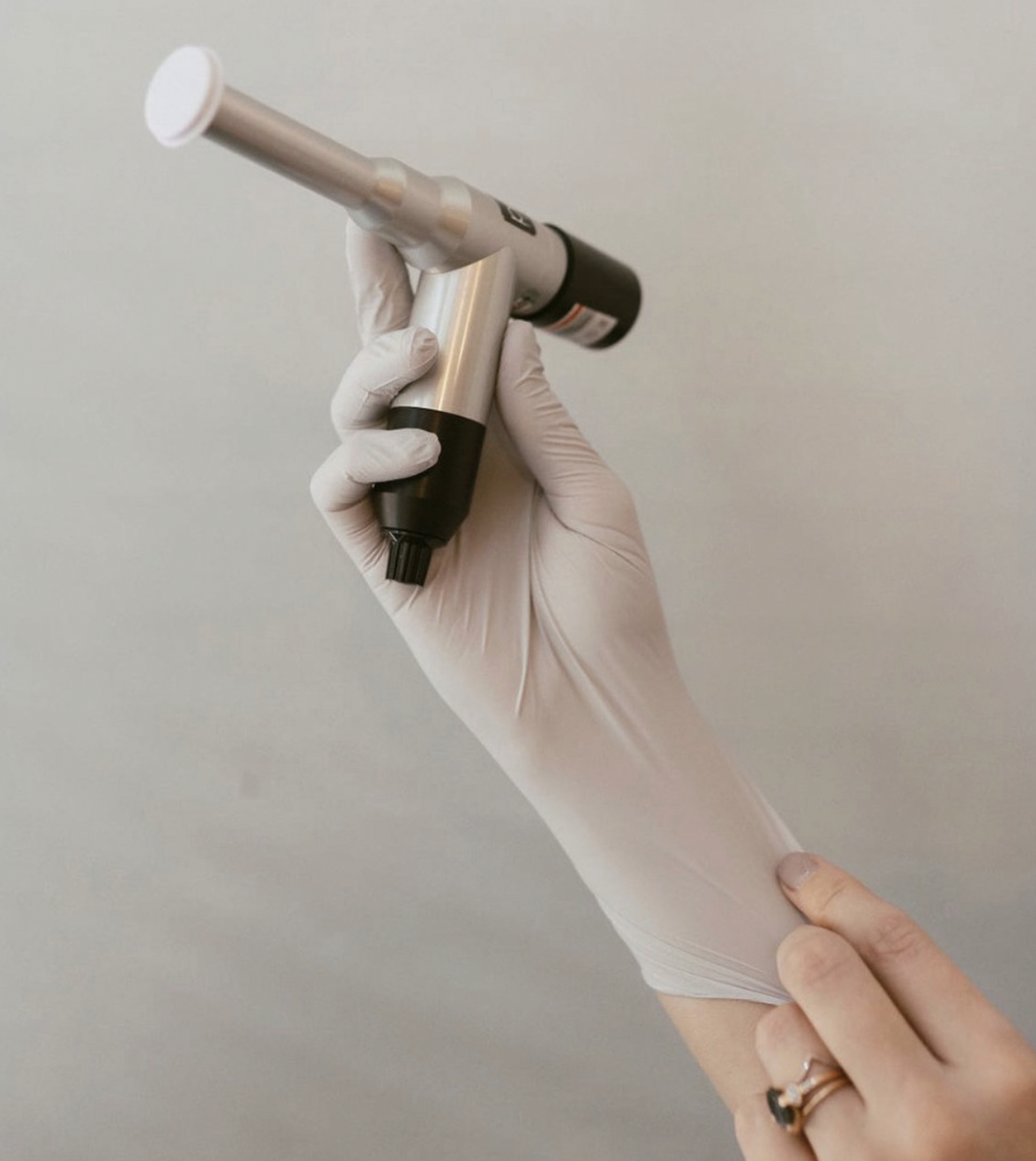 Person wearing latex gloves holding a medical device against a plain background.