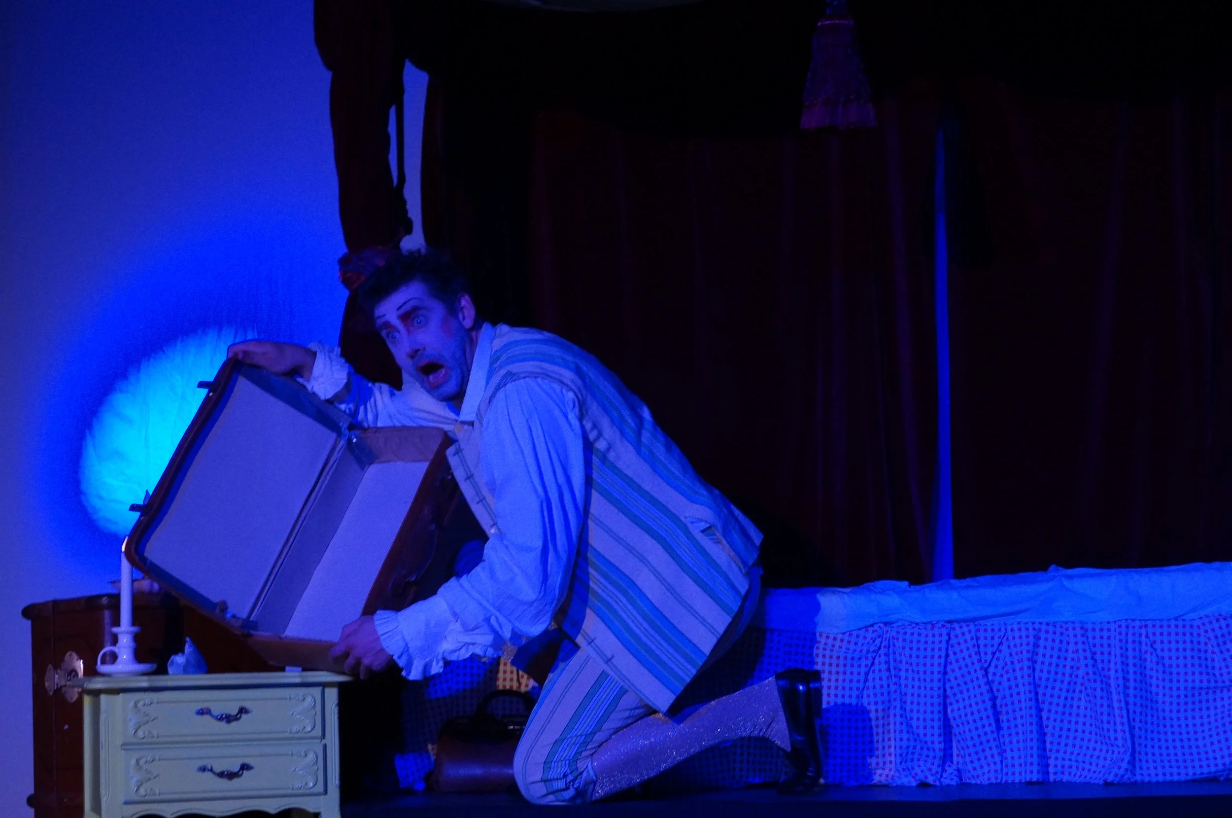 Schauspieler in Panne, der aus einem Koffer aufsteht, in einem Schlafzimmer mit rotem Vorhang und Nachtisch, gespielt auf einer Bühne bei einem Theater.