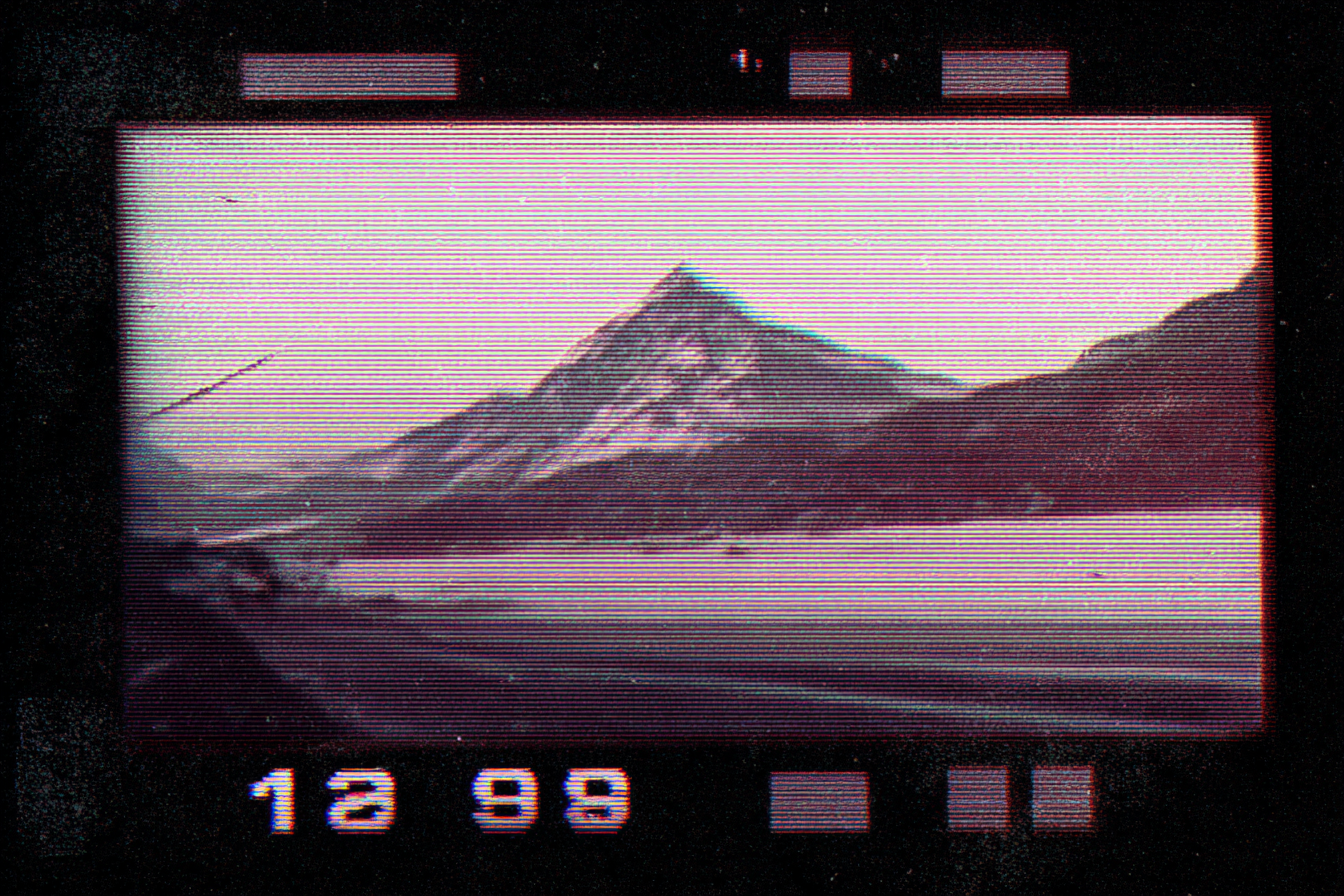 Elderly man looking at a vintage camera screen displaying a mountain landscape with a large peak, possibly the Matterhorn, with a lake in the foreground and snow on the mountain.