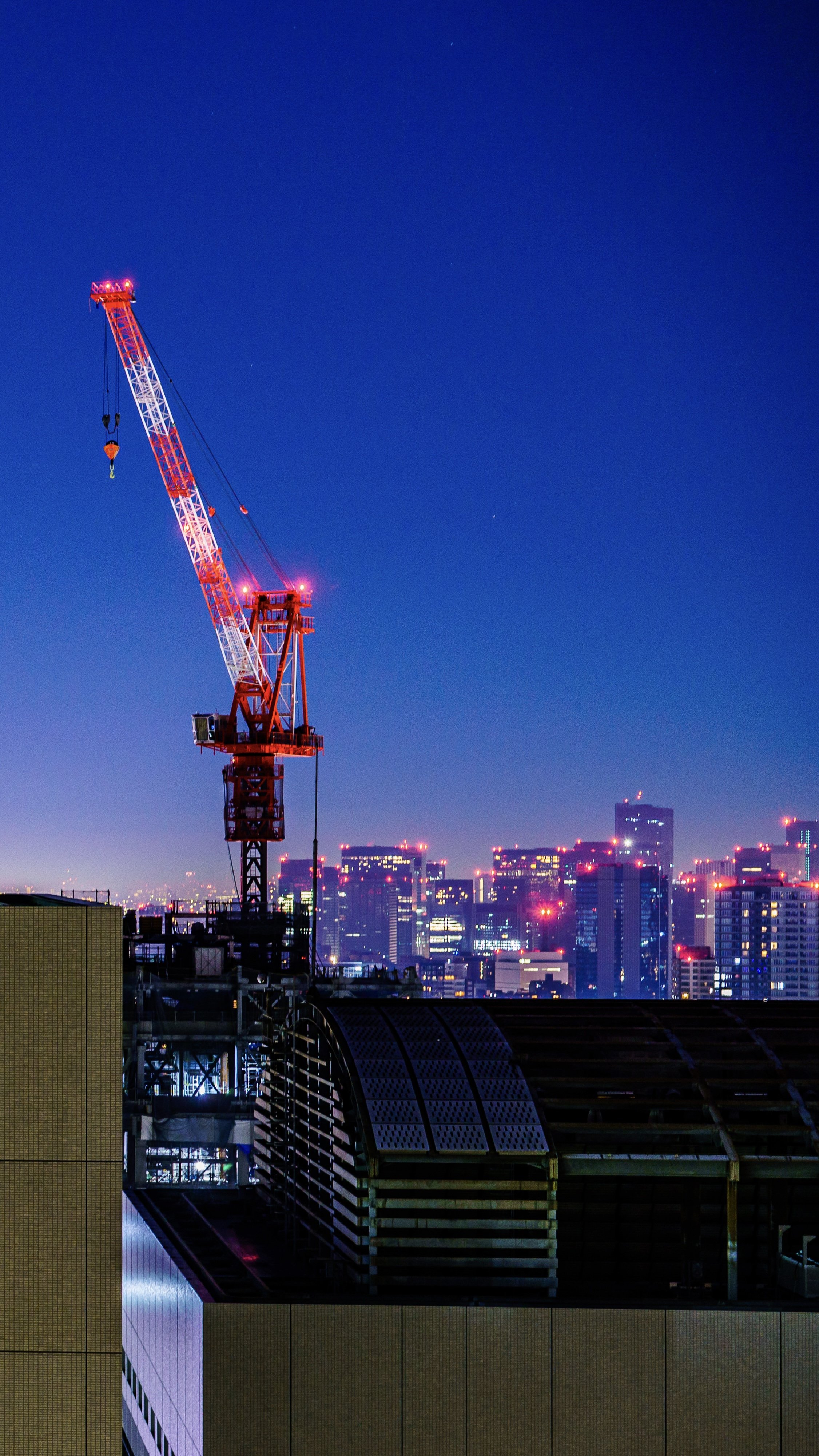 Nighttime cityscape with a red construction crane and illuminated skyscrapers in the background.