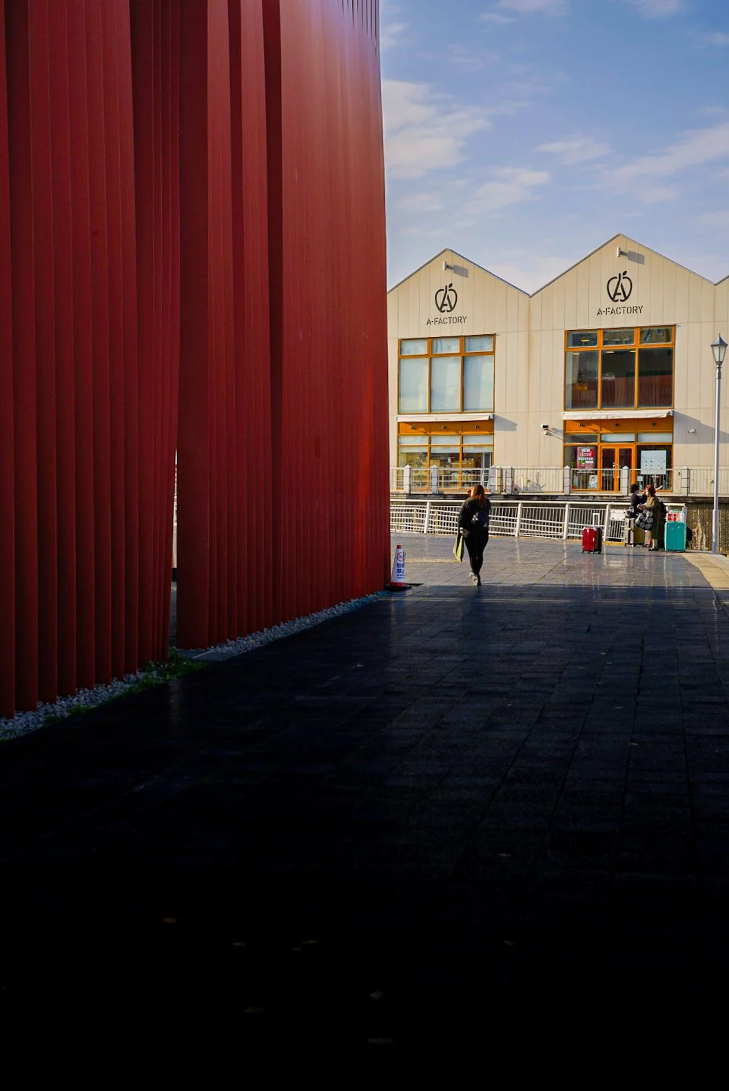 People walking near a modern building with the sign 'A-Factory' on a sunny day.