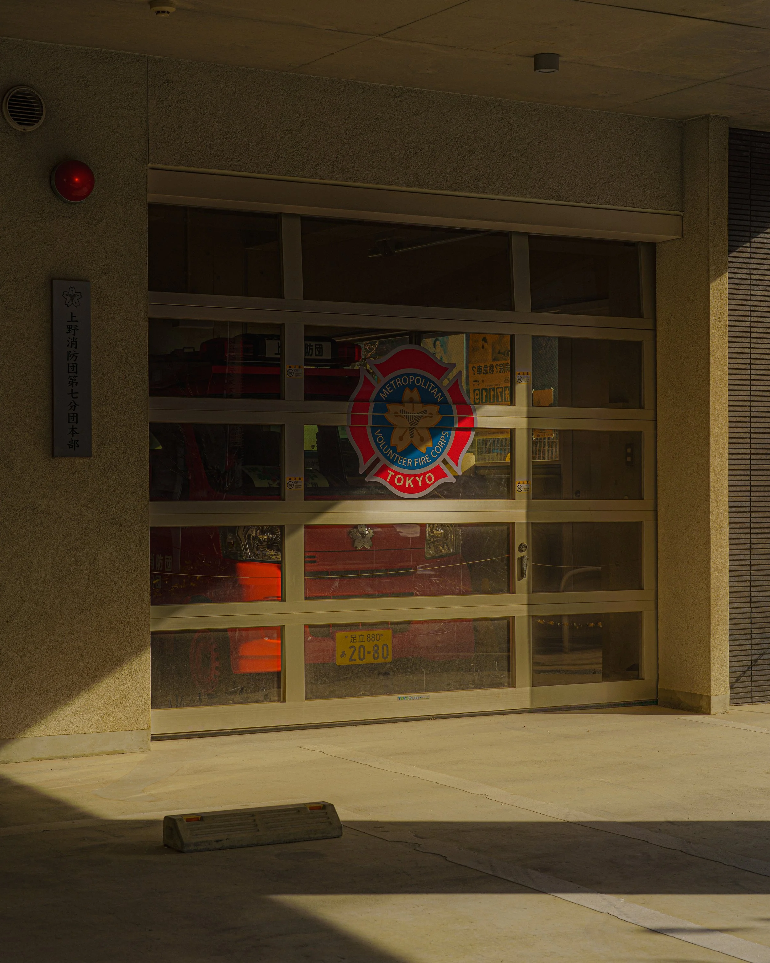 Glass garage door with a Tokyo Metropolitan Volunteer Fire Corps emblem and a red fire truck inside.