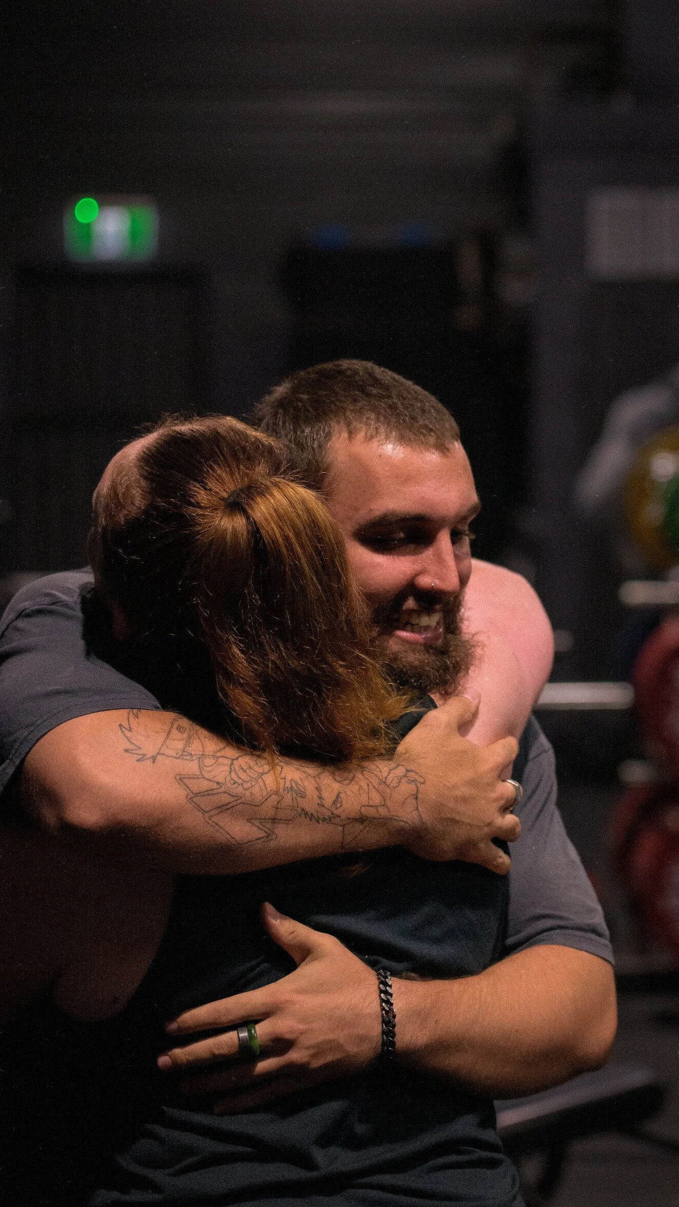 A man and woman hugging, smiling, in a dimly lit environment.