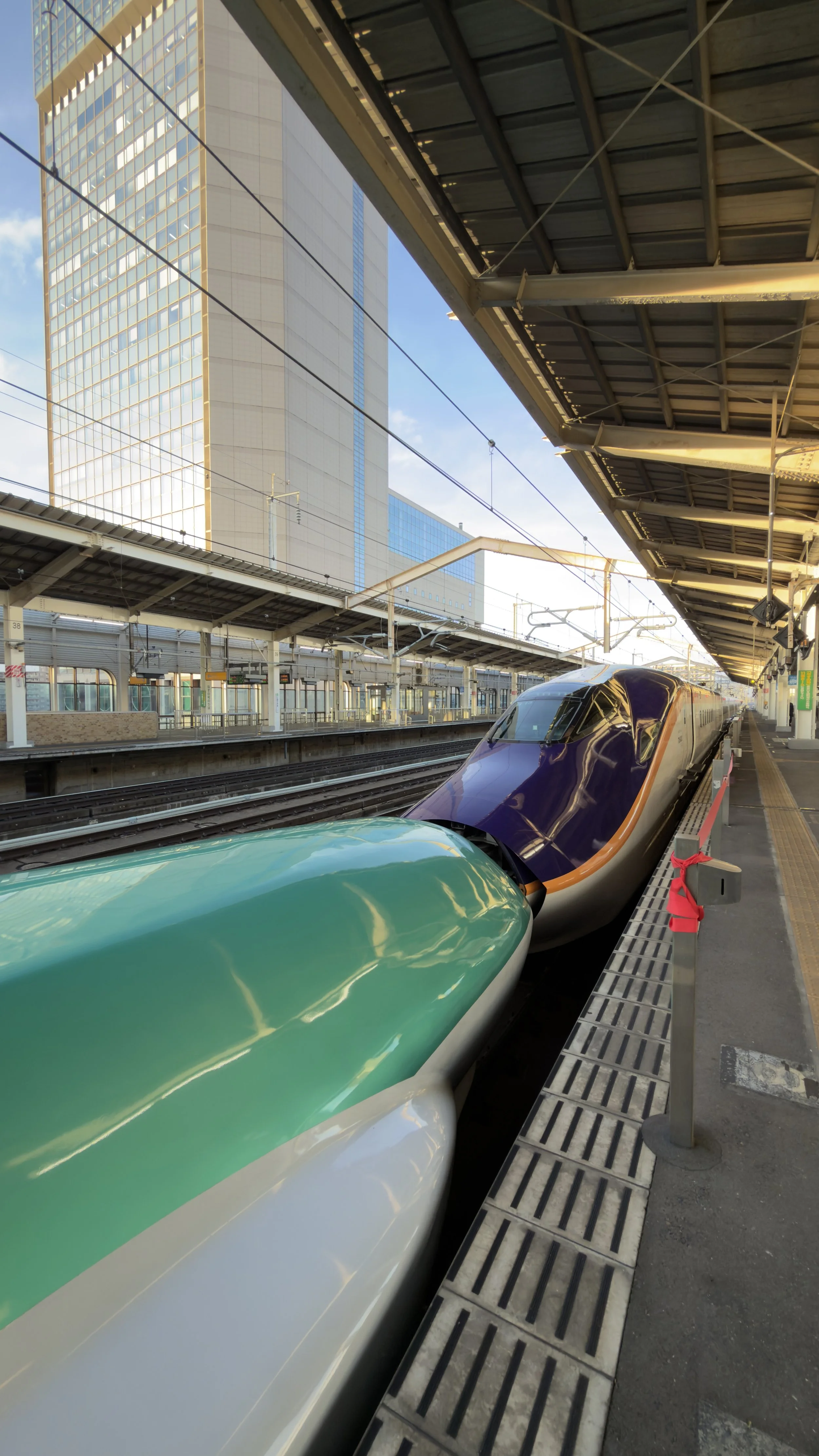 High-speed train at a modern urban train station with high-rise buildings in the background during daytime.