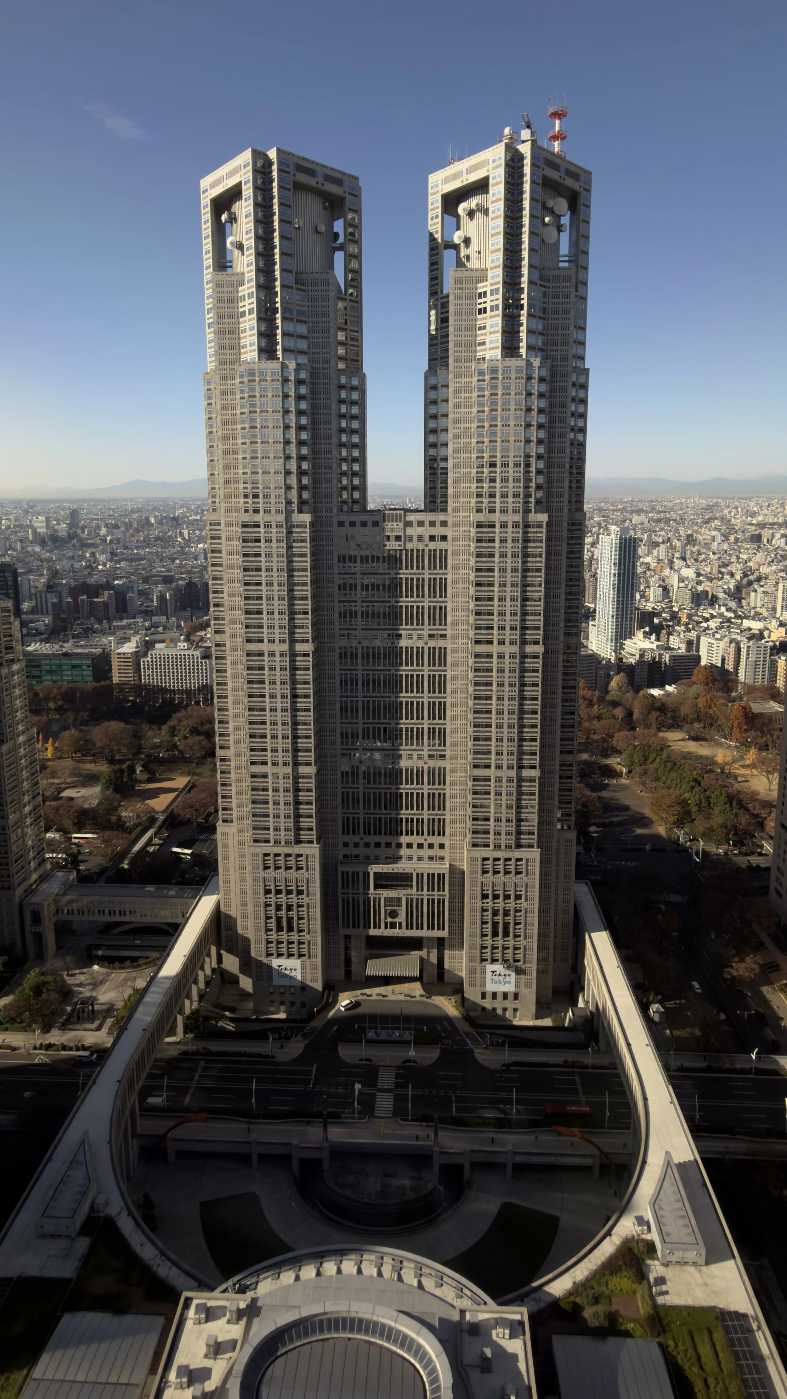 Tall twin towers with a unique architectural design in a cityscape, with the Tokyo Metropolitan Government Building in the foreground, Tokyo, Japan