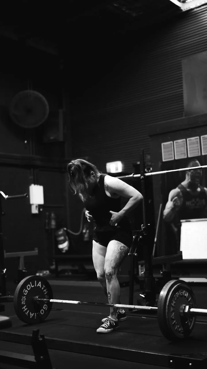 A woman in workout clothes preparing to lift a barbell in a gym.