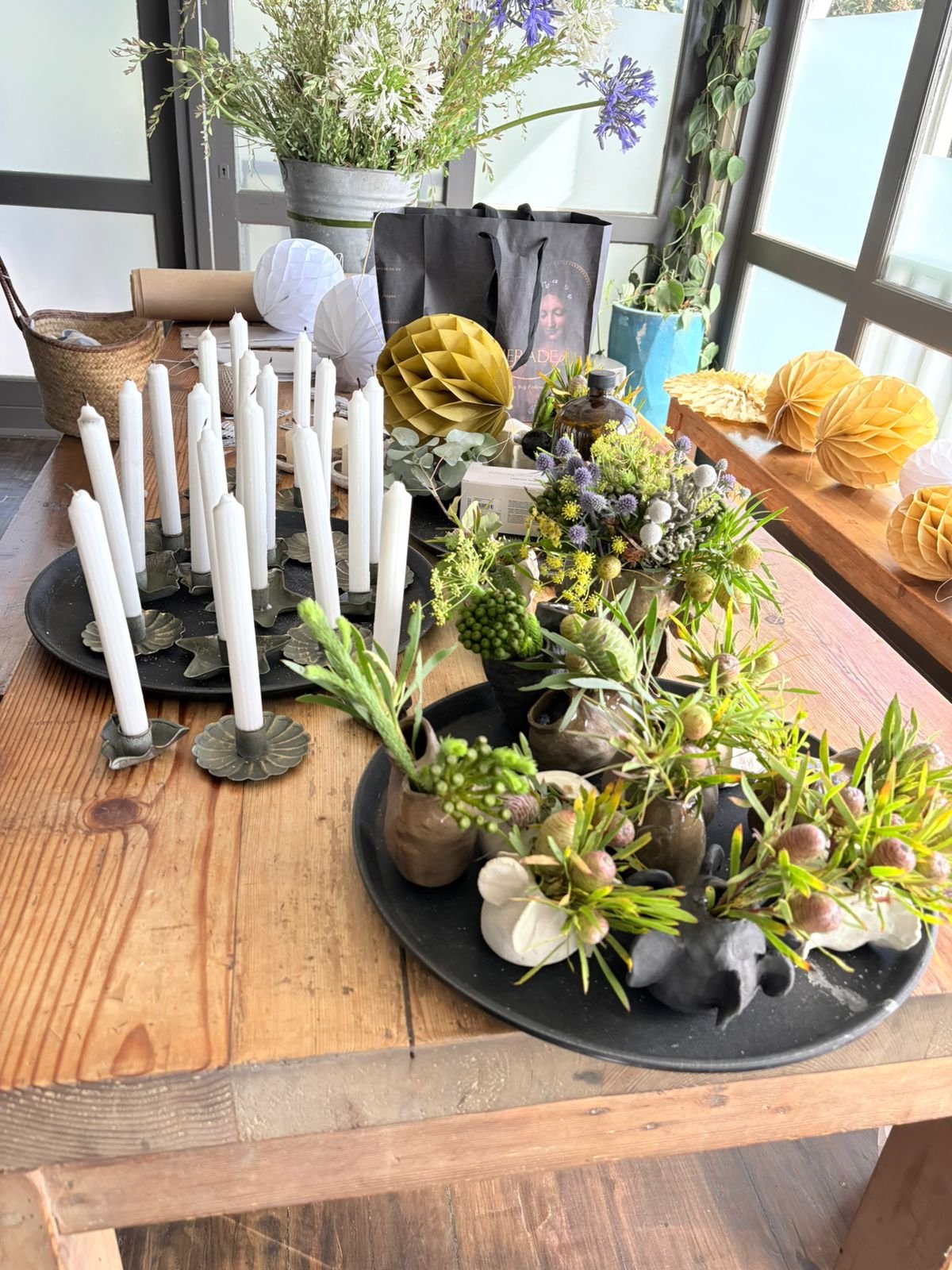 Decorated dining table with candles, flowers, and paper lanterns, with a window and sunlight in the background