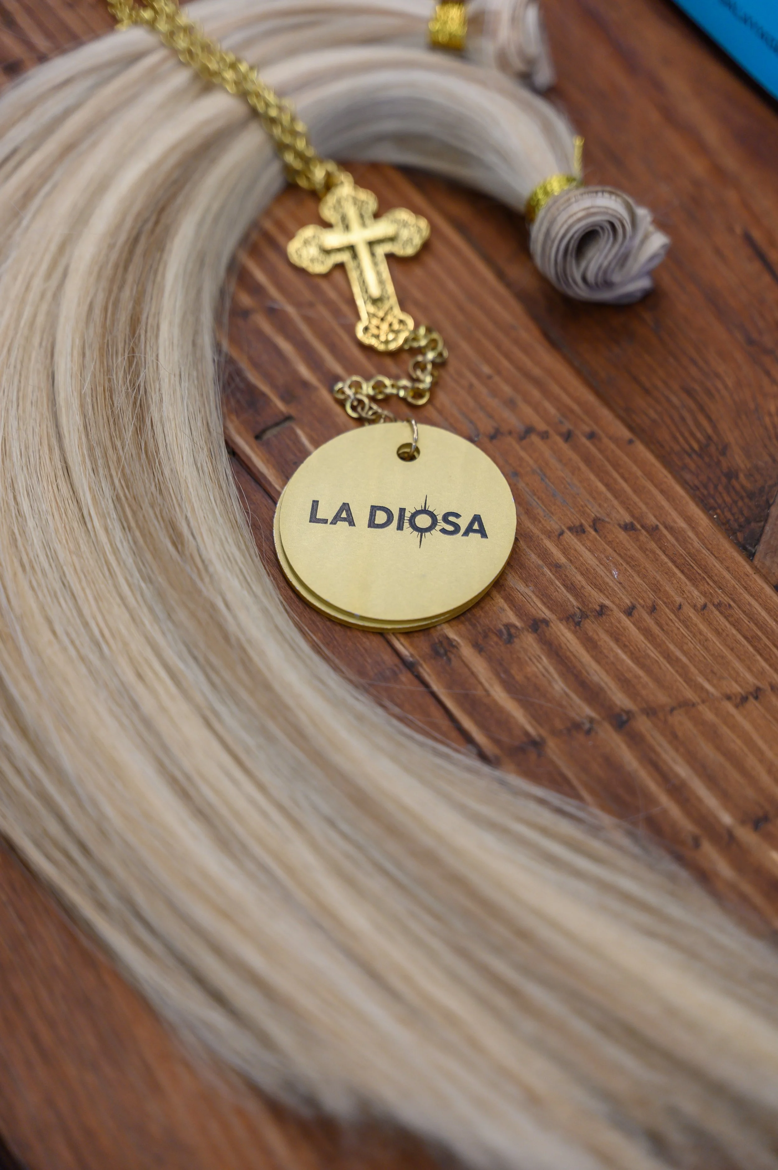 Un rosario con una cruz dorada y un medallón dorado con la inscripción 'La Diosa', sobre una superficie de madera.
